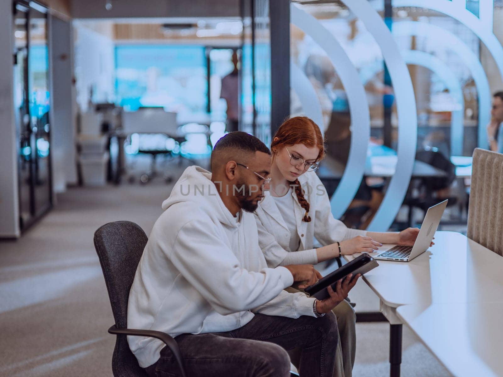 In a modern office setting, an African American businessman and his Muslim colleague, wearing a hijab, engage in collaborative discussions, tackling various business tasks and solving problems together, showcasing diversity, ambition, and teamwork in their dynamic and inclusive workplace