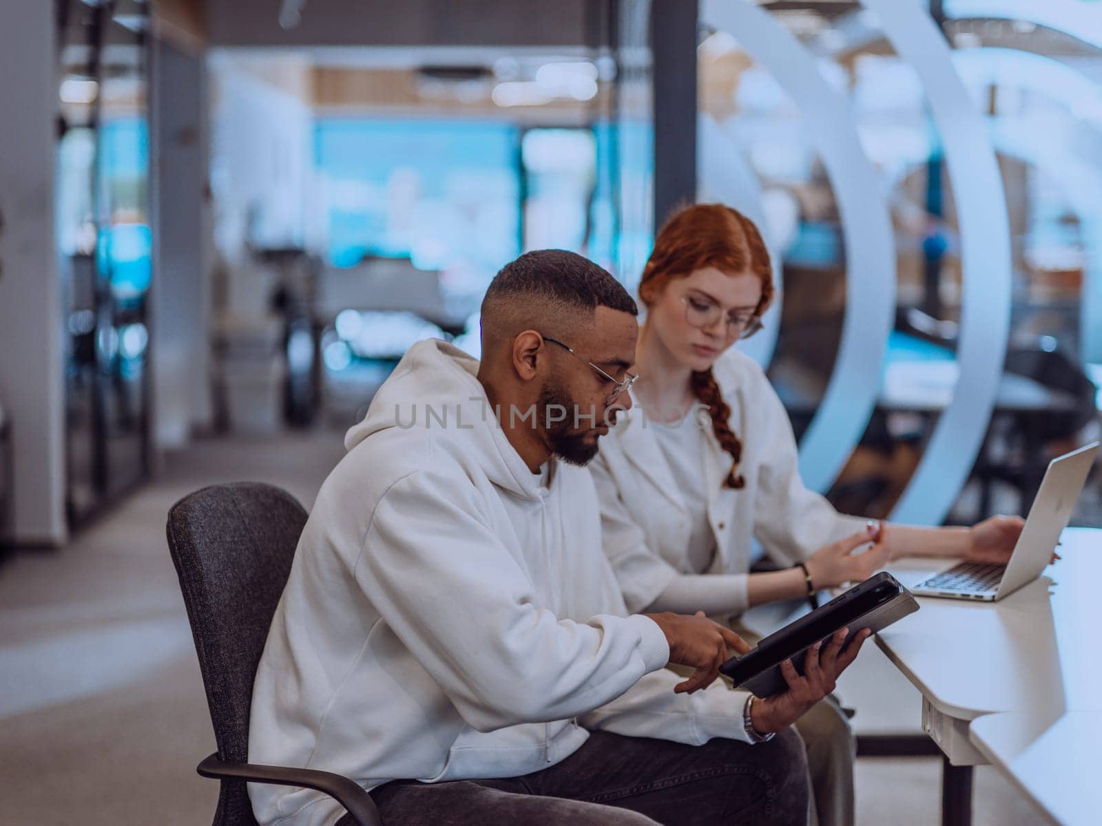 In a modern office setting, an African American businessman and his Muslim colleague, wearing a hijab, engage in collaborative discussions, tackling various business tasks and solving problems together, showcasing diversity, ambition, and teamwork in their dynamic and inclusive workplace. by dotshock