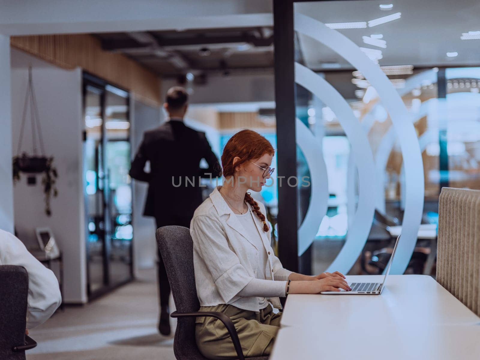 A young businesswoman with orange hair sitting confidently, fully engaged in her work on the laptop, exuding creativity, ambition, and a vibrant sense of individuality.