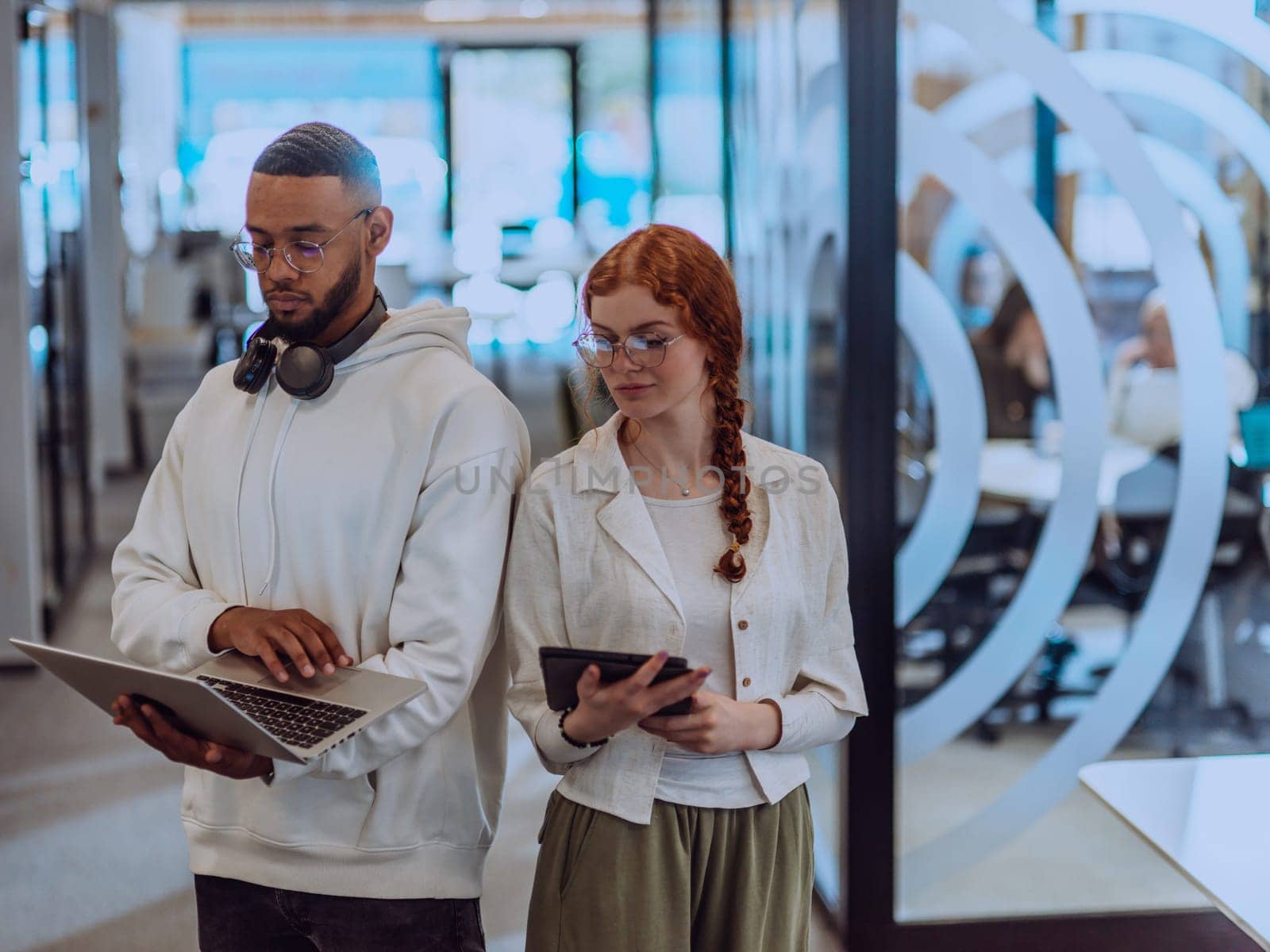 In a modern office African American young businessman and his businesswoman colleague, with her striking orange hair, engage in collaborative problem-solving sessions.