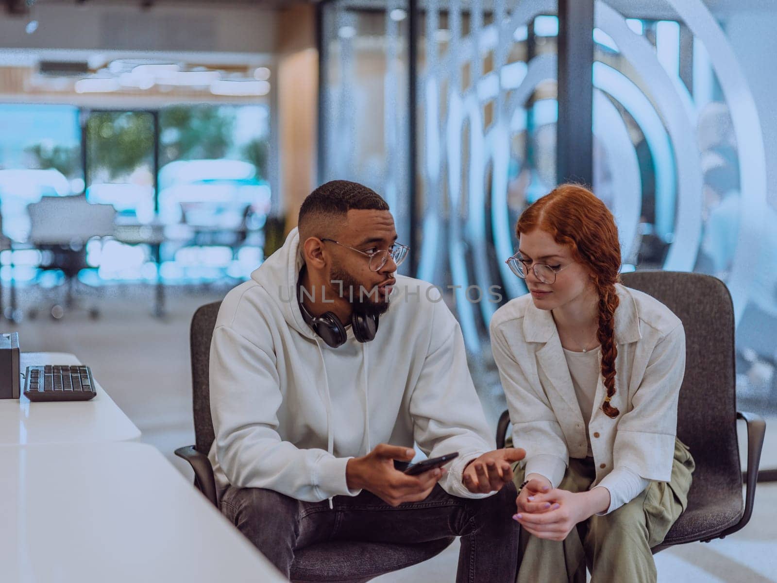 In a modern office African American young businessman and his businesswoman colleague, with her striking orange hair, engage in collaborative problem-solving sessions.