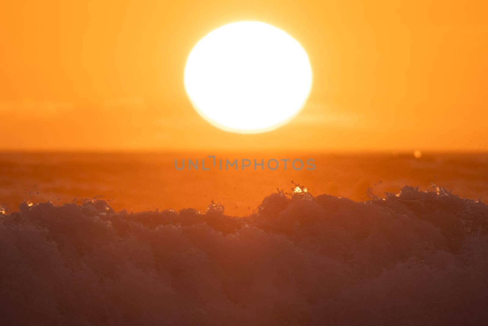 Big sea wave under huge bright sun at orange sunset. Mid shot