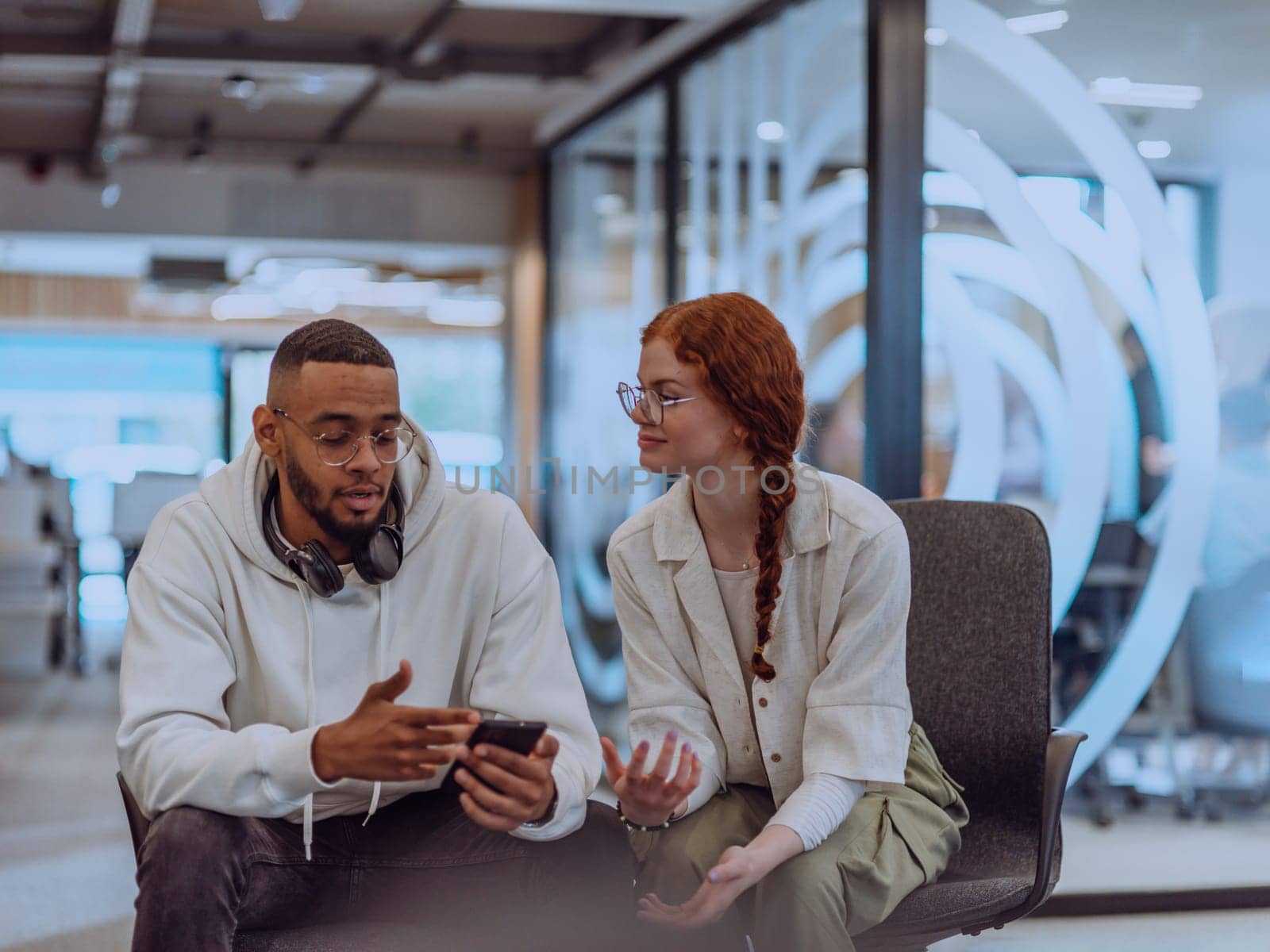 In a modern office African American young businessman and his businesswoman colleague, with her striking orange hair, engage in collaborative problem-solving sessions.