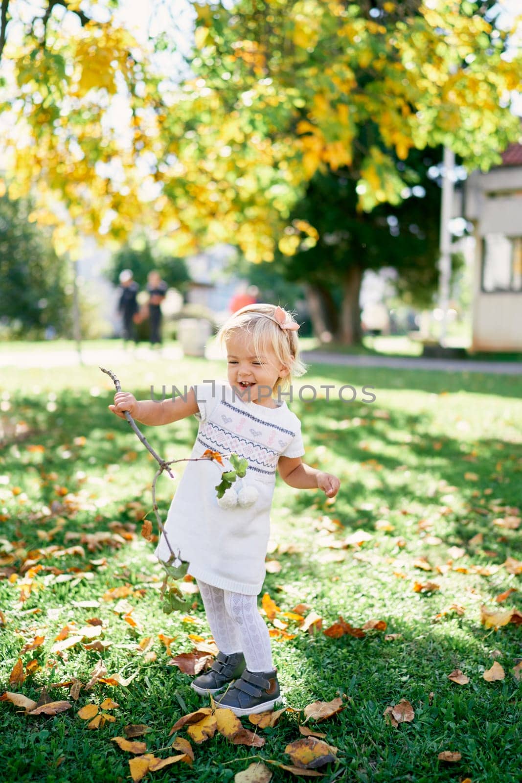 Little smiling girl stands on a green lawn and plays with a tree branch. High quality photo