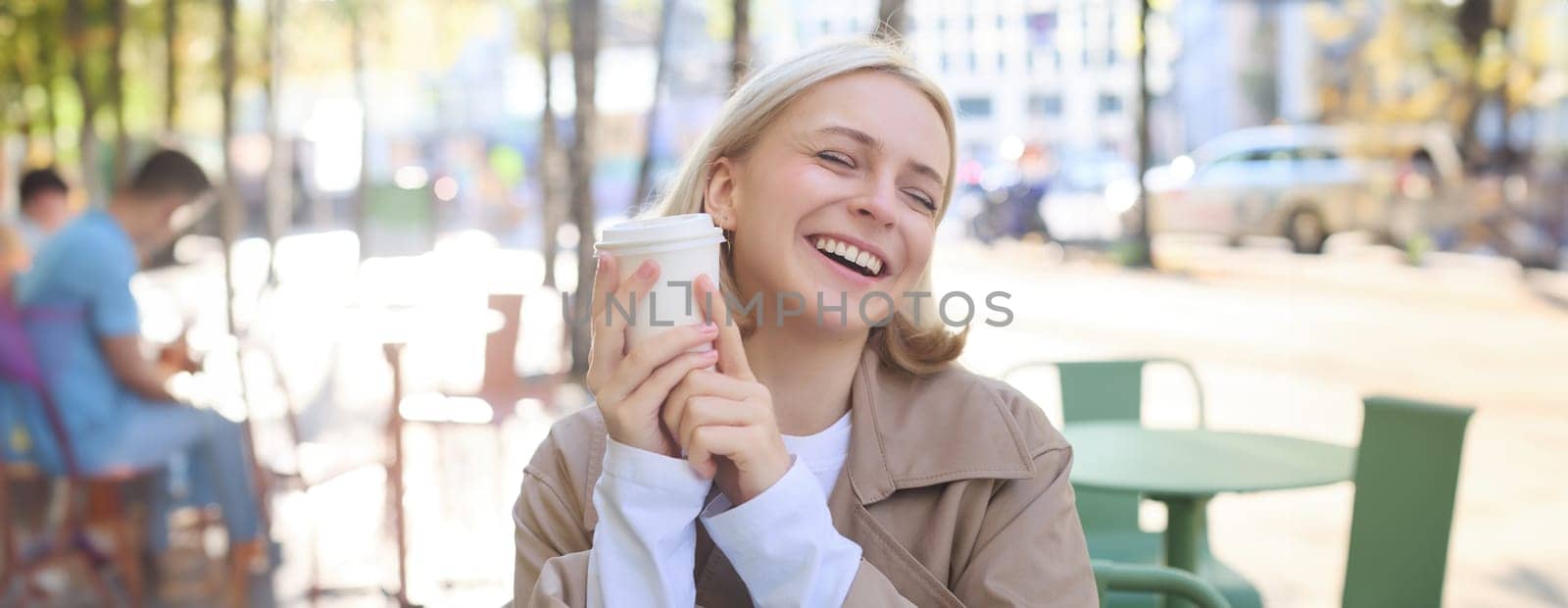 Close up portrait of smiling, happy beautiful european woman, sitting in cafe and enjoying cup of coffee, drinking beverage, enjoying bright sunny day outdoors.