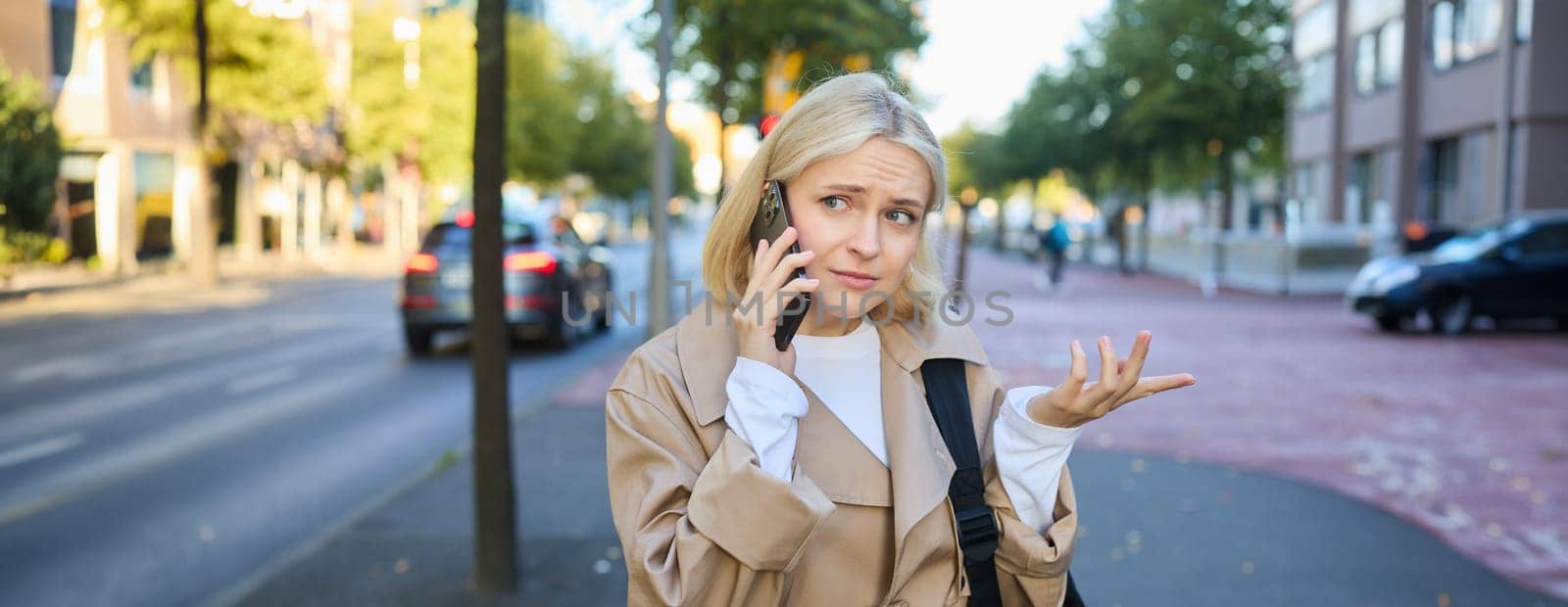 Portrait of woman with confused face, talking on mobile phone, answer phone call, standing on street with puzzled, clueless expression, posing on road.