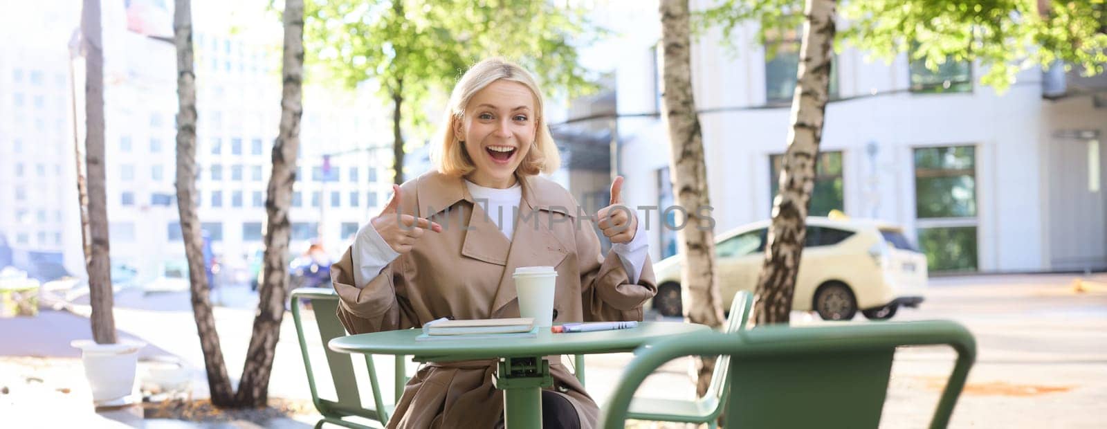 Portrait of excited beautiful girl, pointing fingers at takeaway cup, order awesome drink in cafe, recommending coffee place by Benzoix