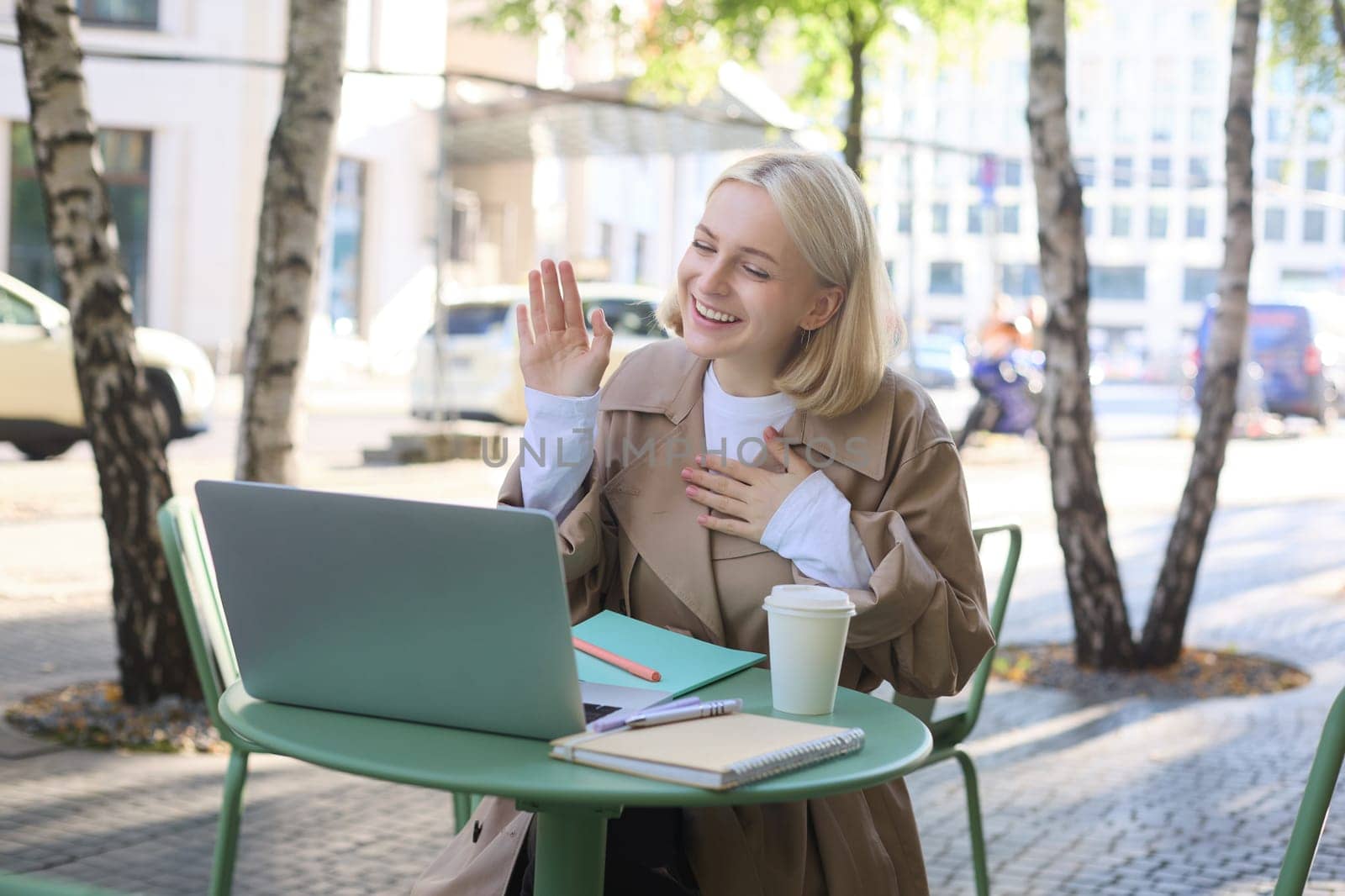 Portrait of young friendly woman, waving hand at laptop and smiling, saying hello, greeting someone, online chatting, having remote conversation while sitting in coffee shop by Benzoix