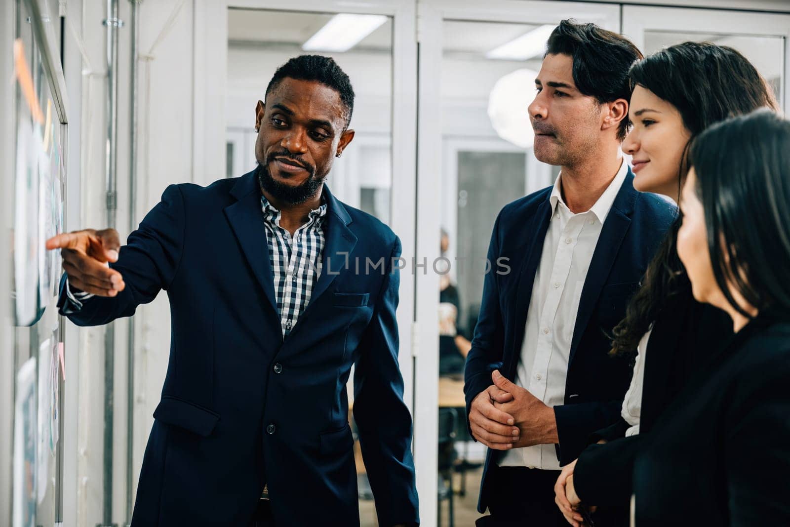 In a dynamic business office setting, colleagues gather around a board. The black businessman leads the discussion, fostering teamwork, brainstorming, and cooperation. team work by Sorapop
