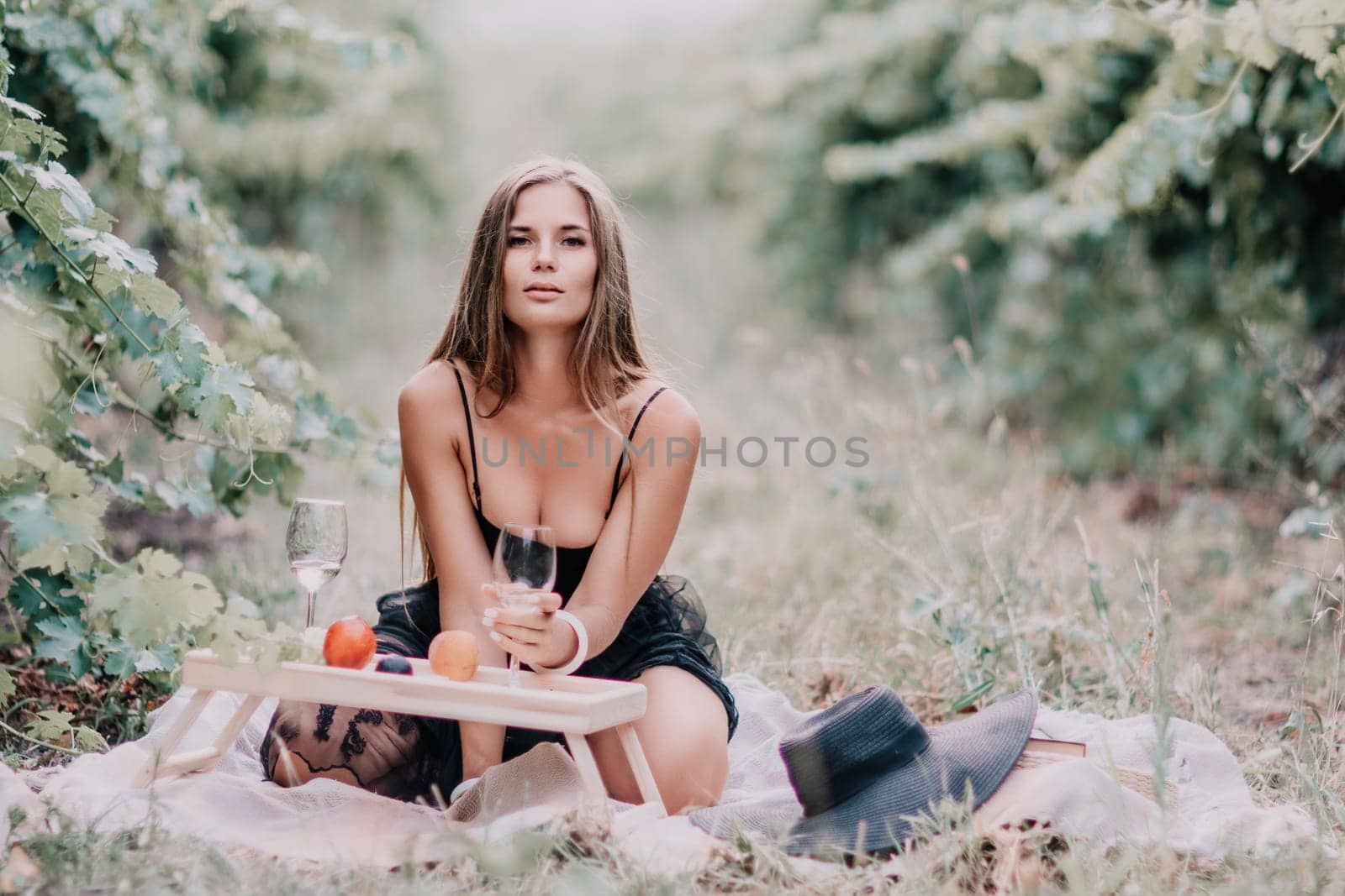 Woman picnic vineyard. Happy woman with a glass of wine at a picnic in the vineyard, wine tasting at sunset and open nature in the summer. Romantic dinner, fruit and wine. by panophotograph