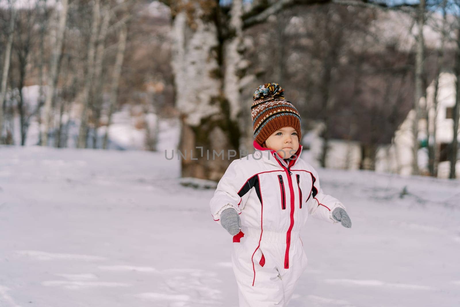 Little girl walks through a snowy forest, pursing her lips by Nadtochiy