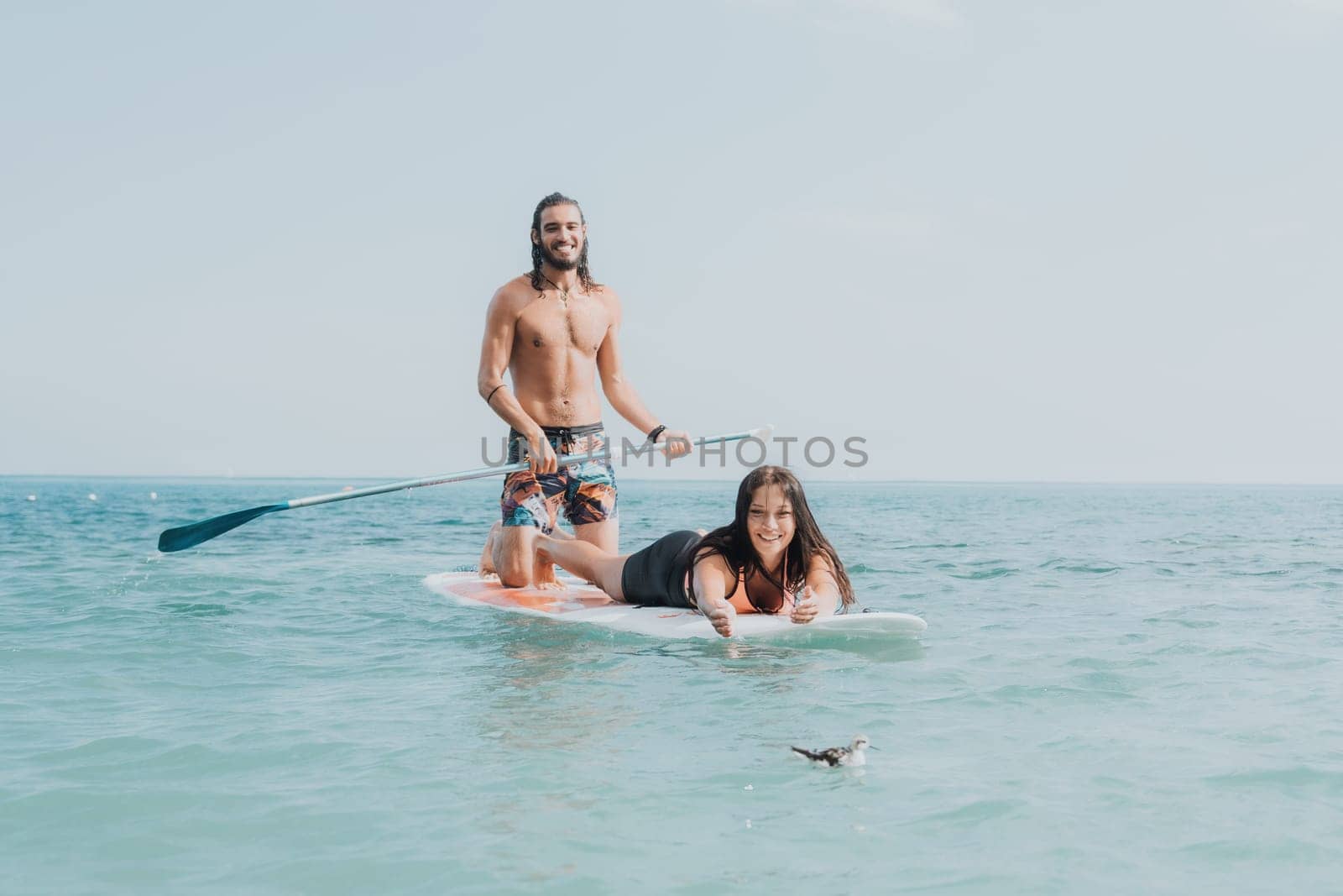Sea woman and man on sup. Silhouette of happy young woman and man, surfing on SUP board, confident paddling through water surface. Idyllic sunset. Active lifestyle at sea or river