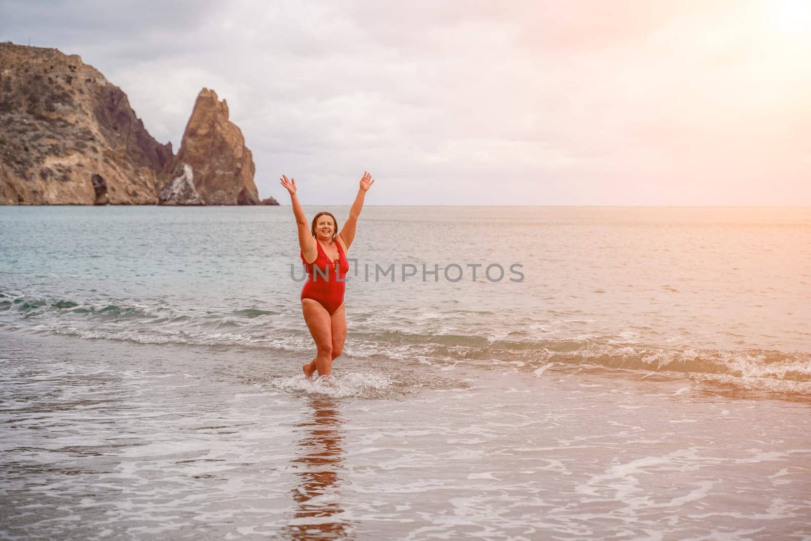 Woman in a bathing suit at the sea. A fat young woman in a red swimsuit enters the water during the surf.