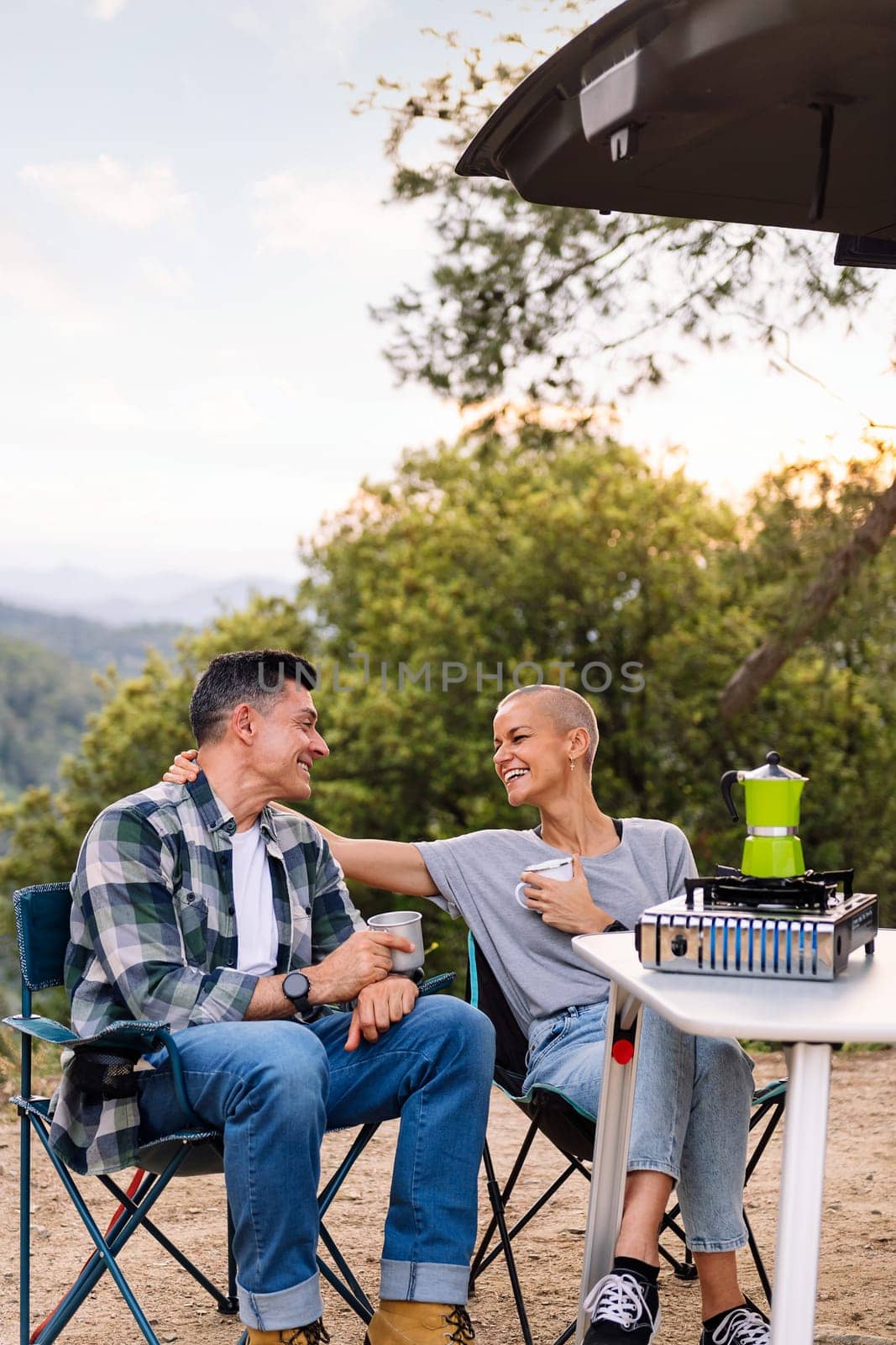 happy couple laughing while having coffee in the countryside, concept of active tourism in nature and outdoor activities, copy space for text