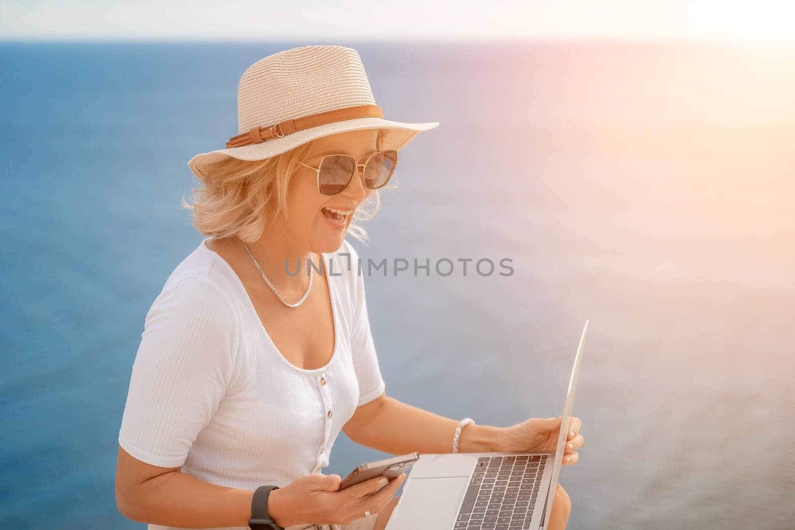 Freelance women sea working on the computer. Good looking middle aged woman typing on a laptop keyboard outdoors with a beautiful sea view. The concept of remote work