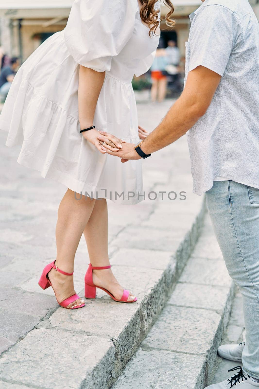 Woman leaned towards man holding her hands while standing on the steps. Cropped. Faceless. High quality photo
