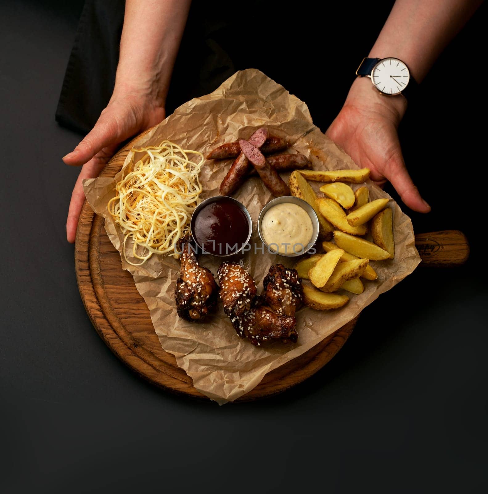 beer snacks - grilled wings with sauce french fries on a wooden board on a black background by aprilphoto