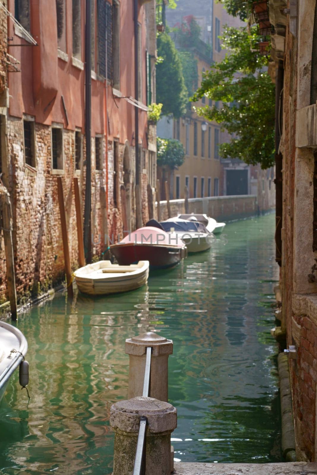 Sunny channel in Venice with boats parked around. Venice, Veneto region, Italy - September 2023: Canal in Venice. Traditional architecture of Venice by aprilphoto