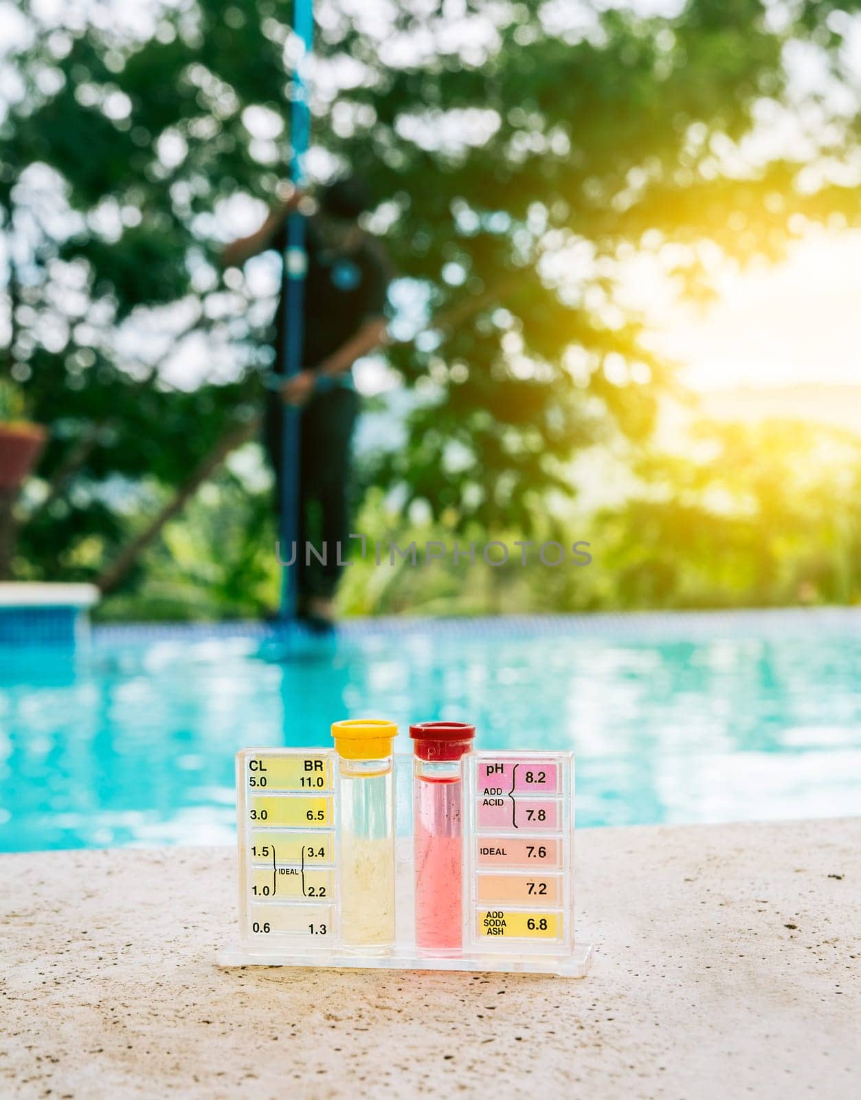 Water PH tester kit on the edge of the swimming pool with maintenance person in the background by isaiphoto