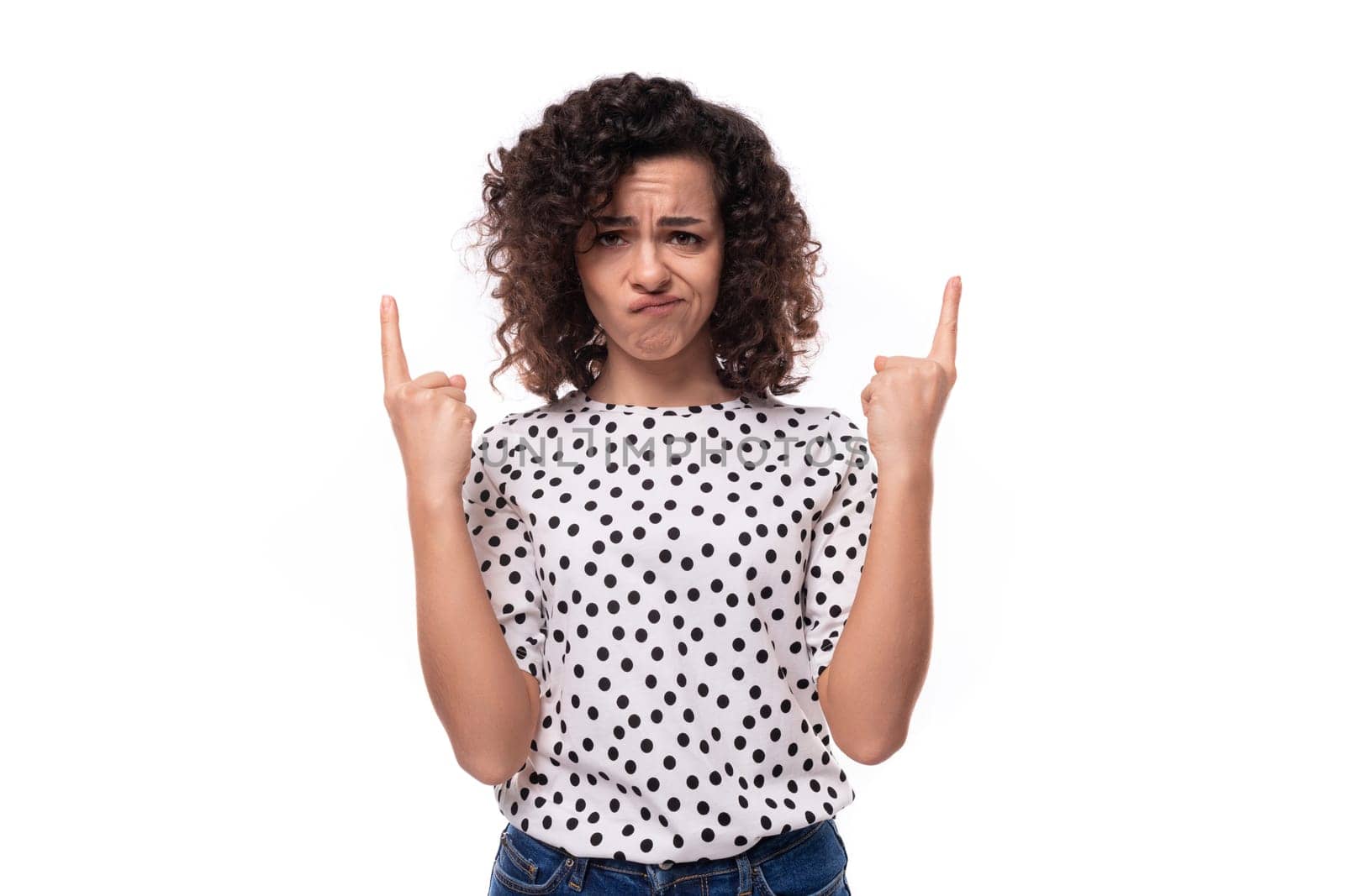 a young woman with a curly hairstyle dressed in a summer blouse with a polka dot print shows her hands on an empty space.