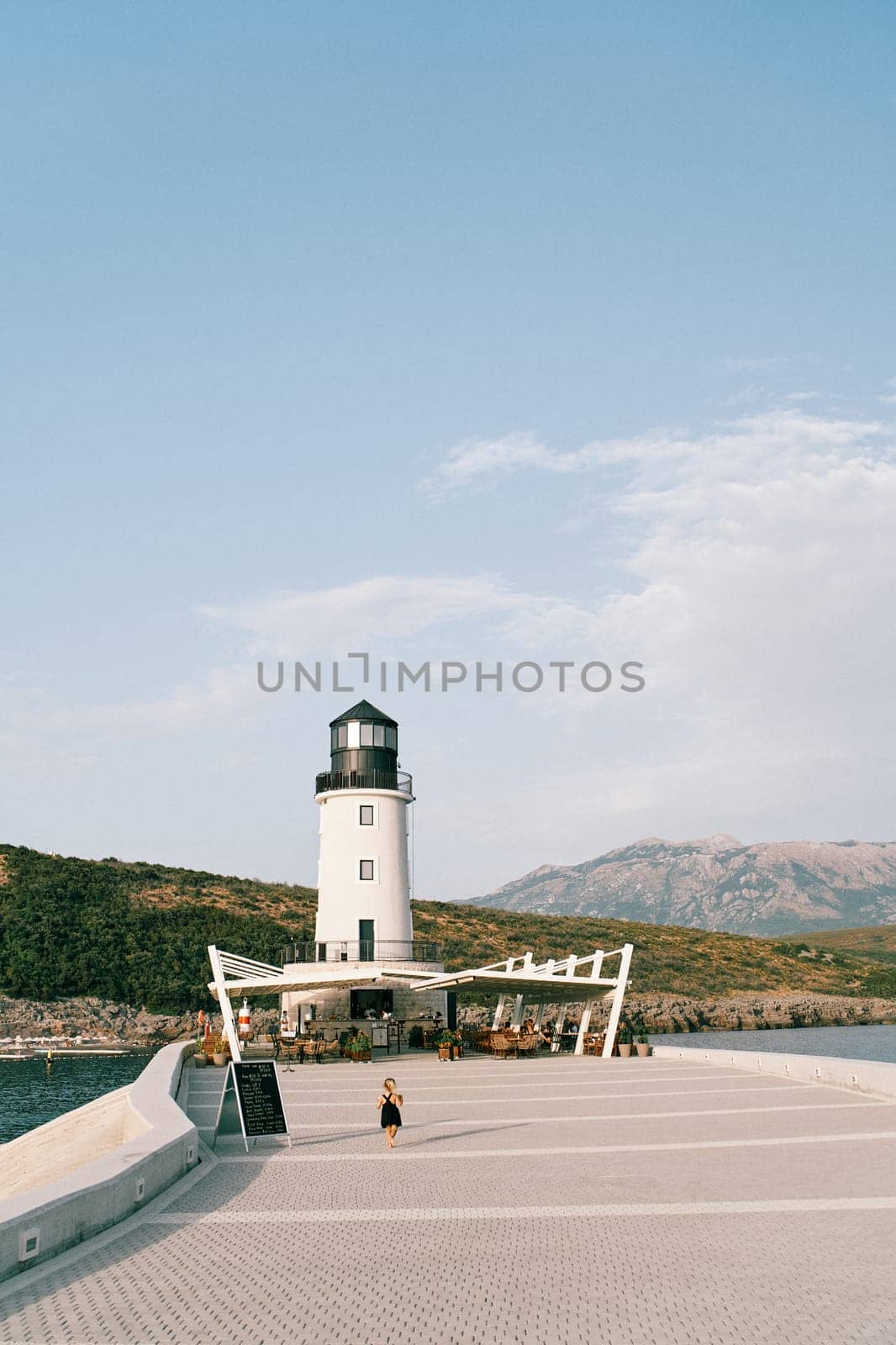 Little girl walks along the pier against the backdrop of a lighthouse with an outdoor restaurant. High quality photo