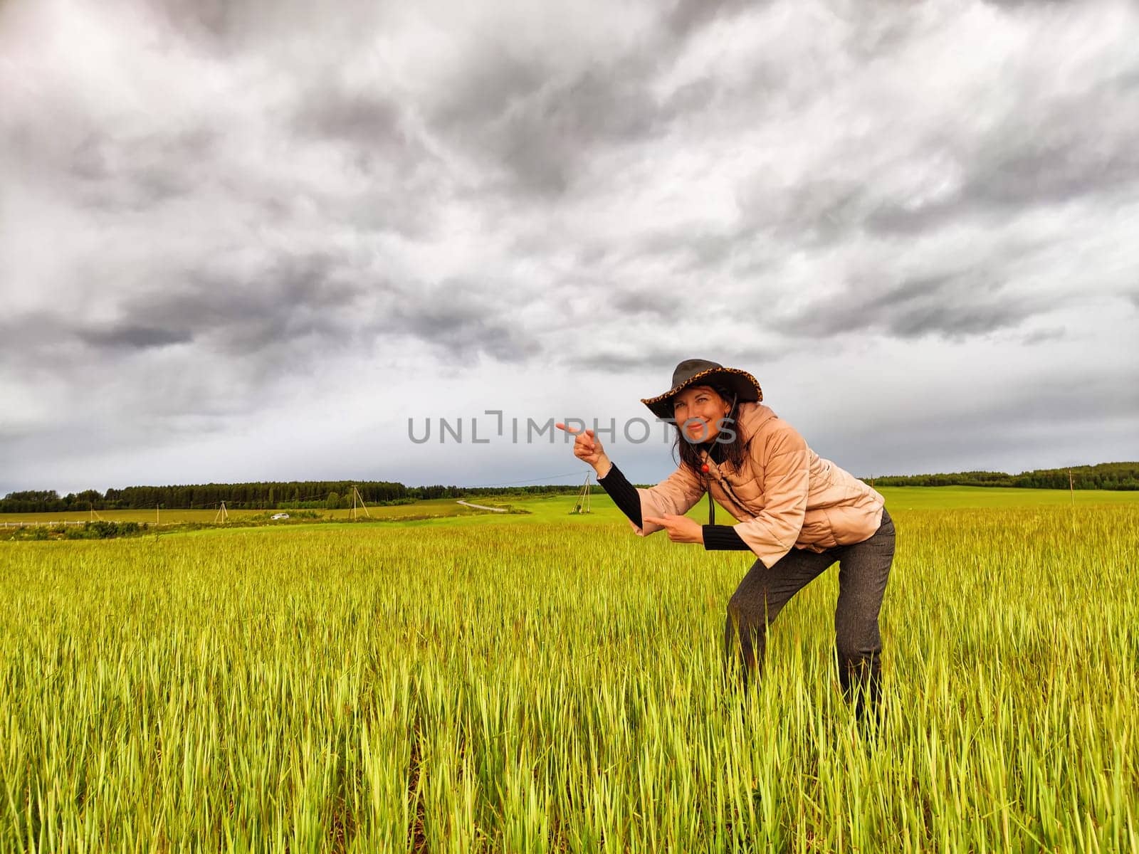 An adult girl looking like a cowboy in a hat in a field and with a stormy sky with clouds takes pictures of a rainbow and takes selfie in the rain. Woman having fun outdoors on rural and rustic nature by keleny