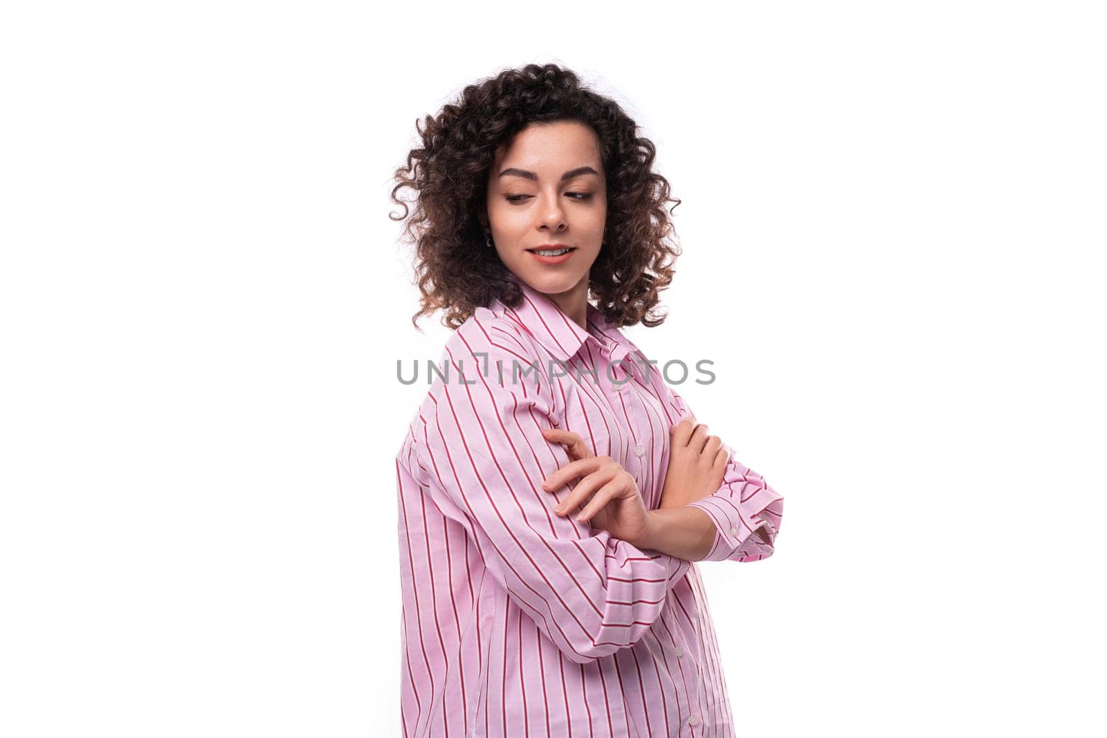 portrait of a 30 year old authentic slim curly brunette model woman wearing a pink shirt.