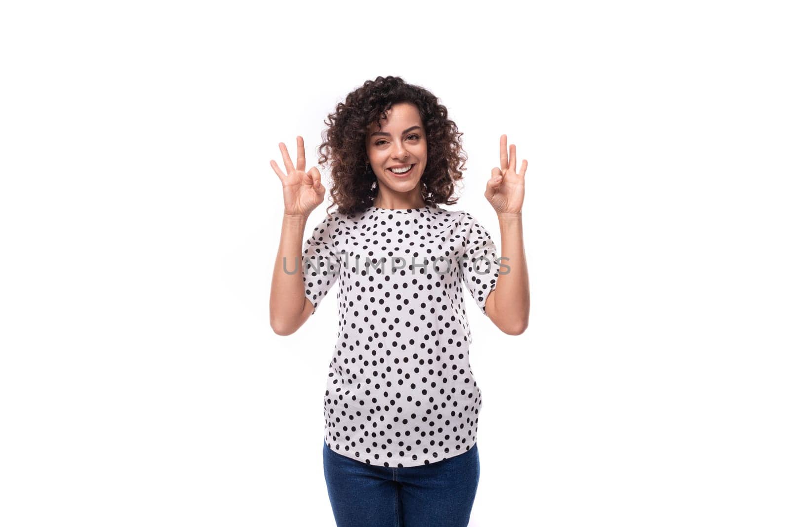 charming young brunette curly woman dressed in summer blouse with pea print shows gesture ok by TRMK