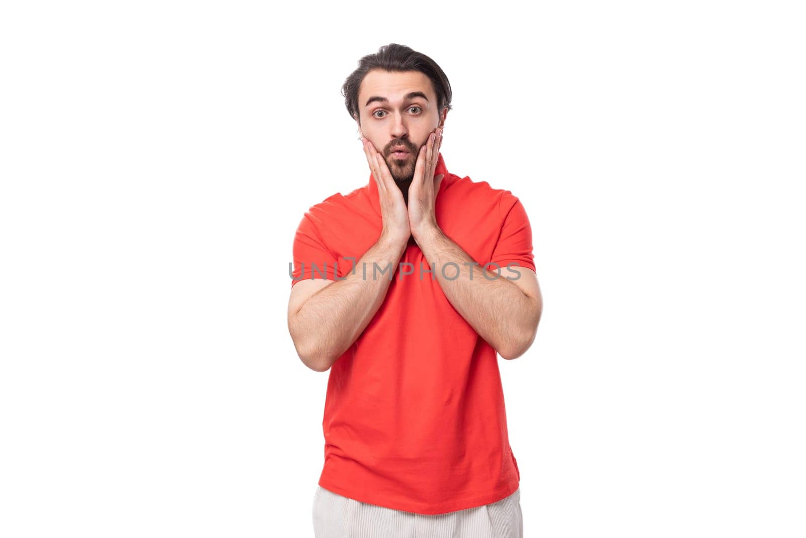 young surprised european brunette man with a beard dressed in a red t-shirt on a white background with copy space. photo for promo by TRMK