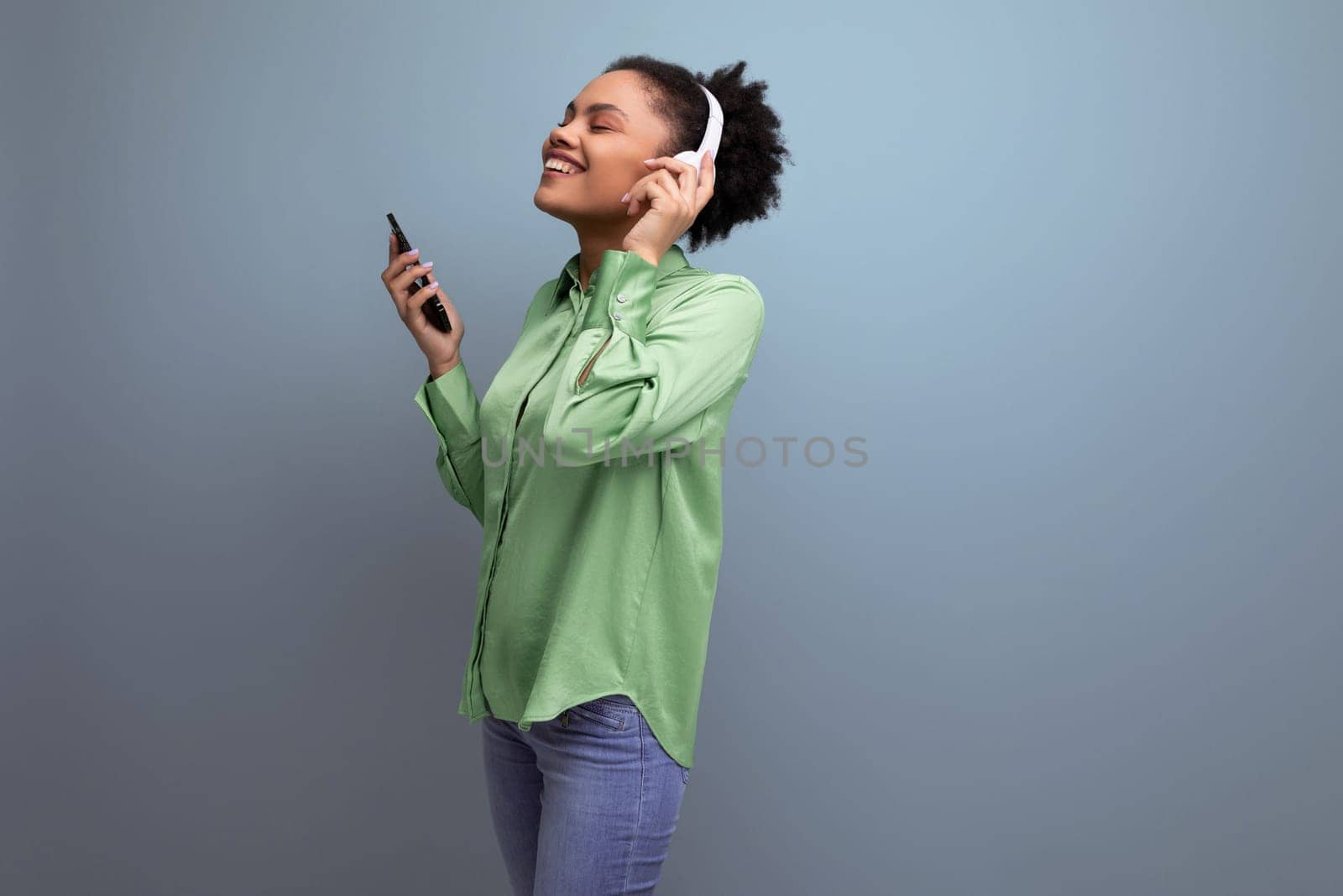 young energetic music lover latin business lady in green blouse listening to music with headphones on studio background with copy space.