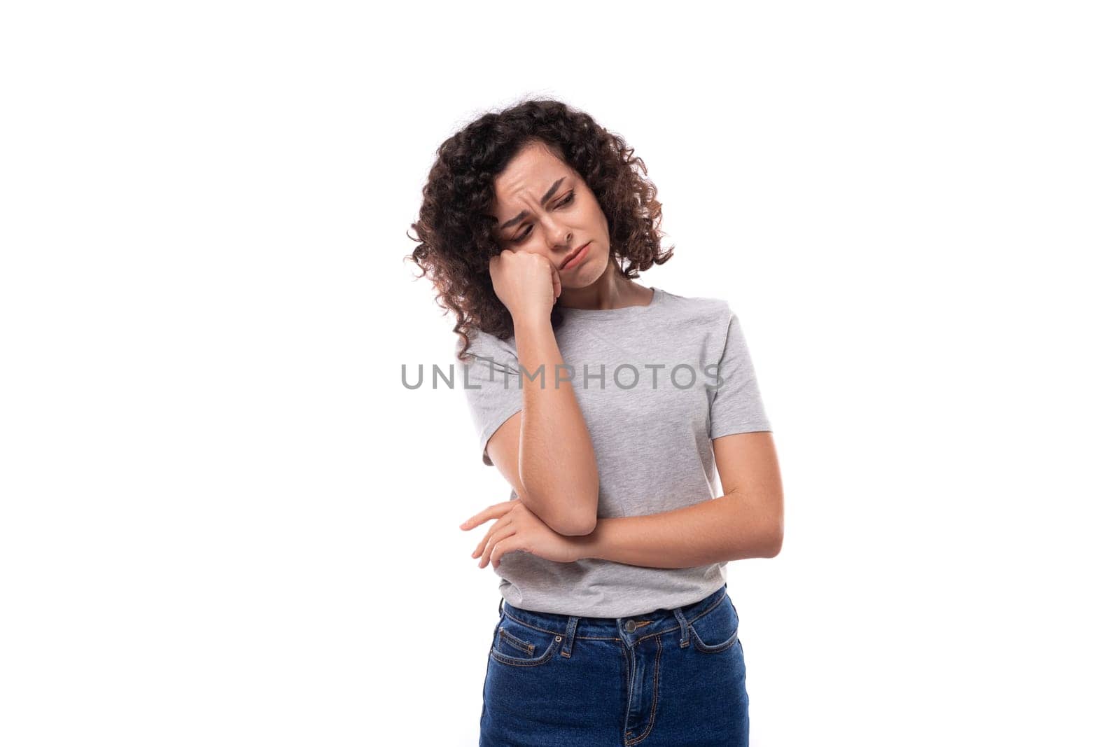 young tired slender 30 year old caucasian woman with curly hair in a gray t-shirt on a white background with copy space by TRMK