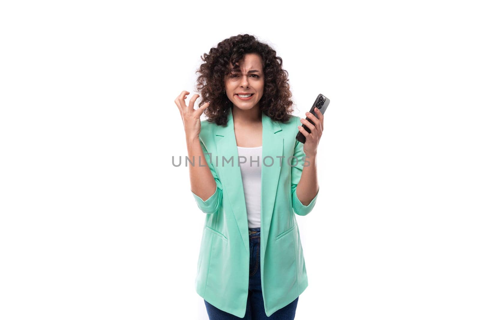 young excited curly brunette employee of a business company woman dressed in an office blue jacket holding a phone by TRMK