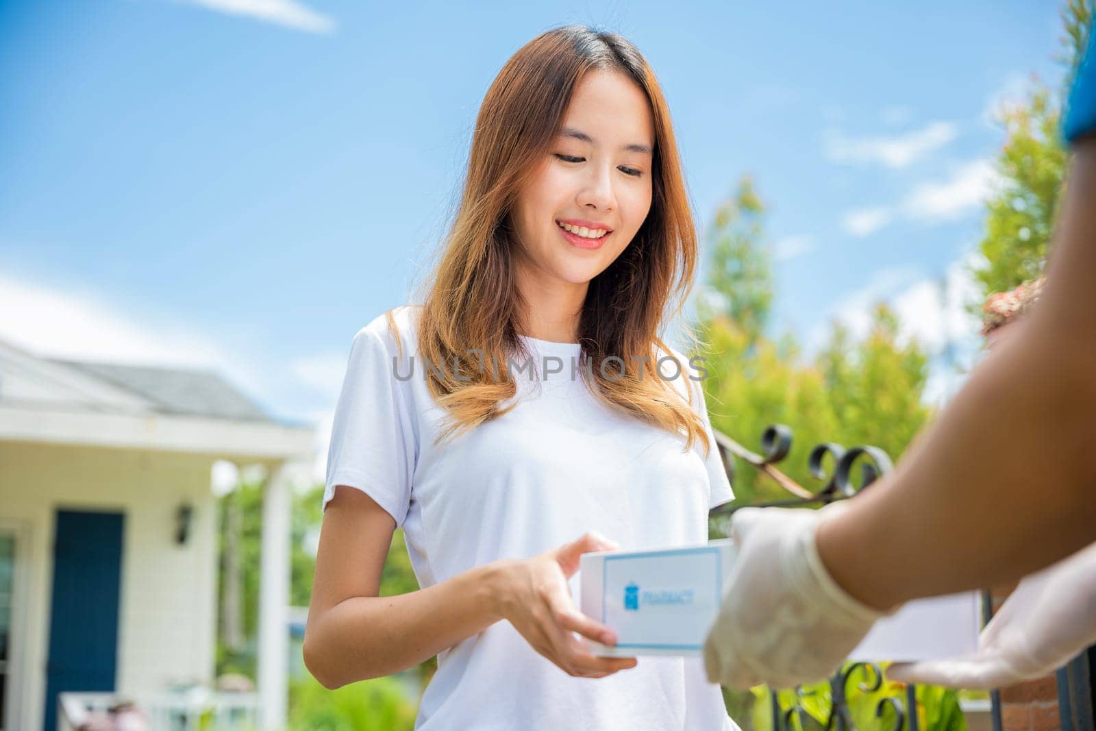 Sick Asian woman hand hold for receive medication first aid pharmacy box from hospital delivery service at front home, merchandise medicine, Delivery man give medicine drug store to patient female