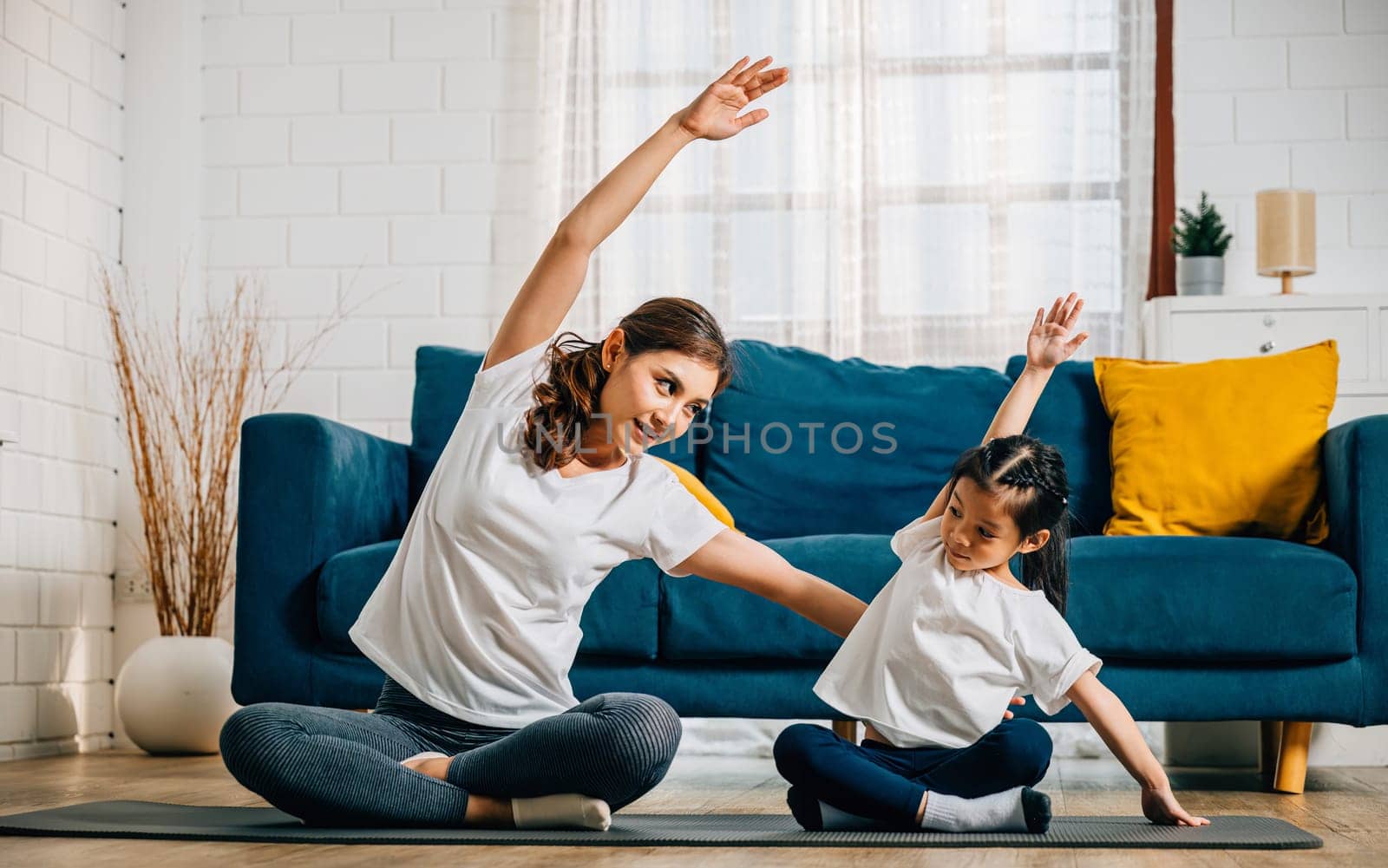 A mother teaches her daughter yoga focusing on stretch and balance in their home by Sorapop