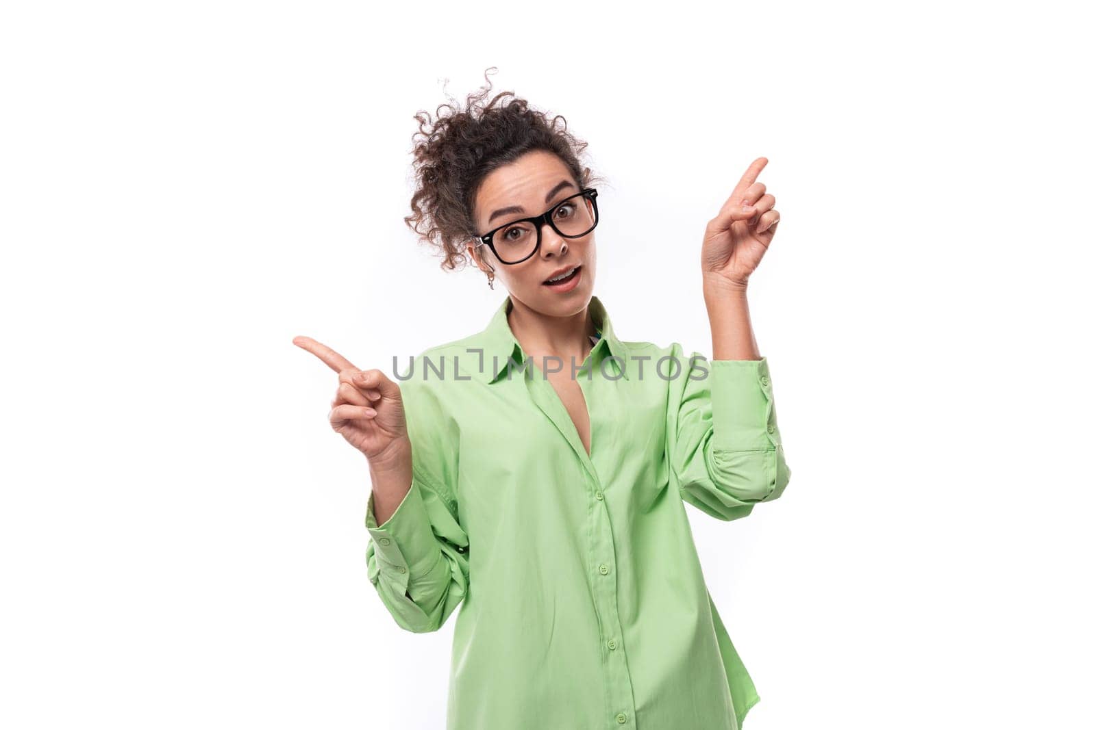 pretty young brunette curly woman in glasses is dressed in a green shirt on a white background with copy space by TRMK