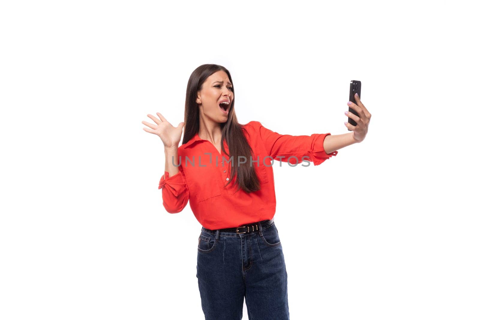 portrait of a charming young model woman with straight black hair dressed in a red blouse chatting on smartphone video call.