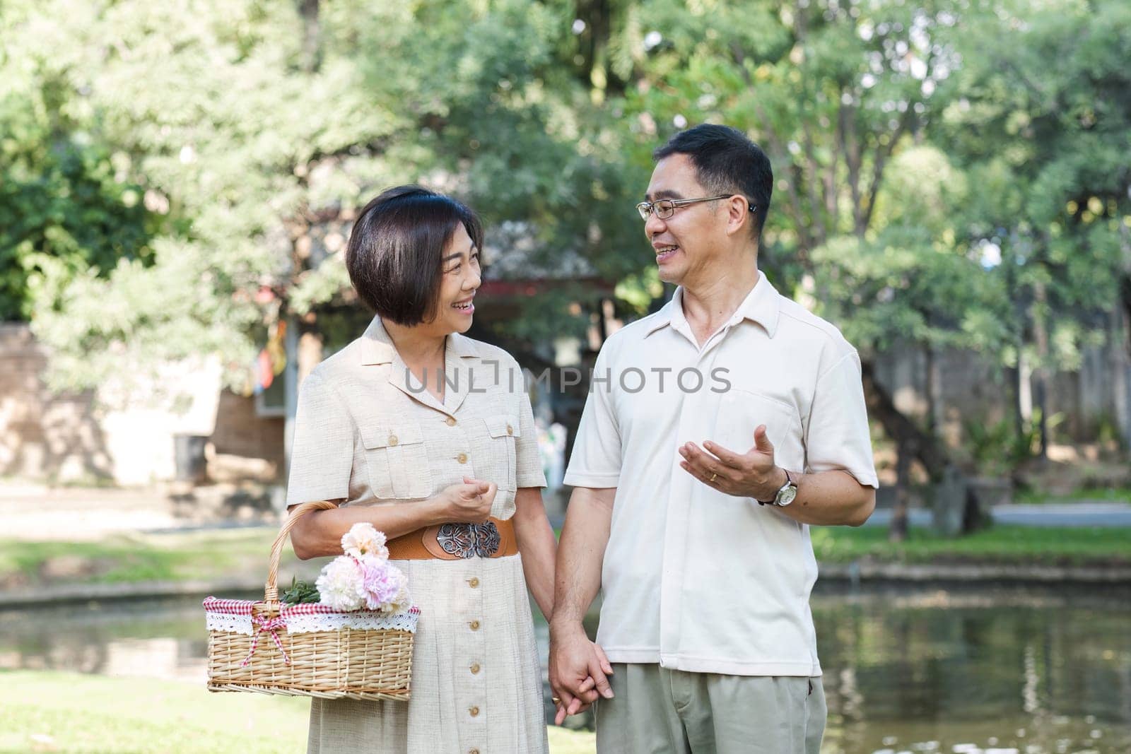 Senior man and wife holding a picnic basket walking among the green trees in the park A retired couple in their 60s walked through the garden together enjoying their vacation..