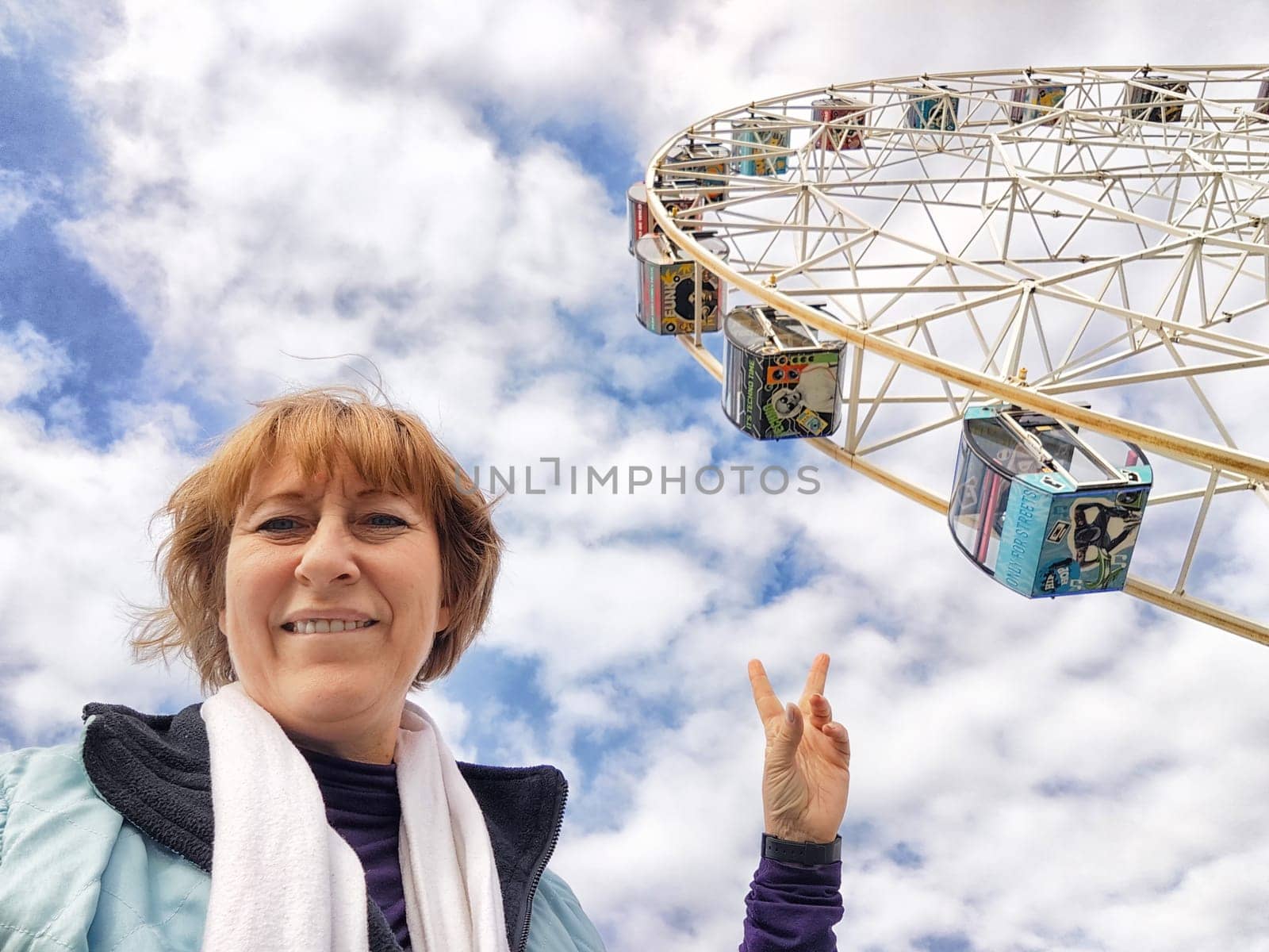 Relaxed mature caucasian female making selfie outside near big Ferris wheel. Positive senior woman against city street. Adult middle agged girl Blogger taking photo for internet