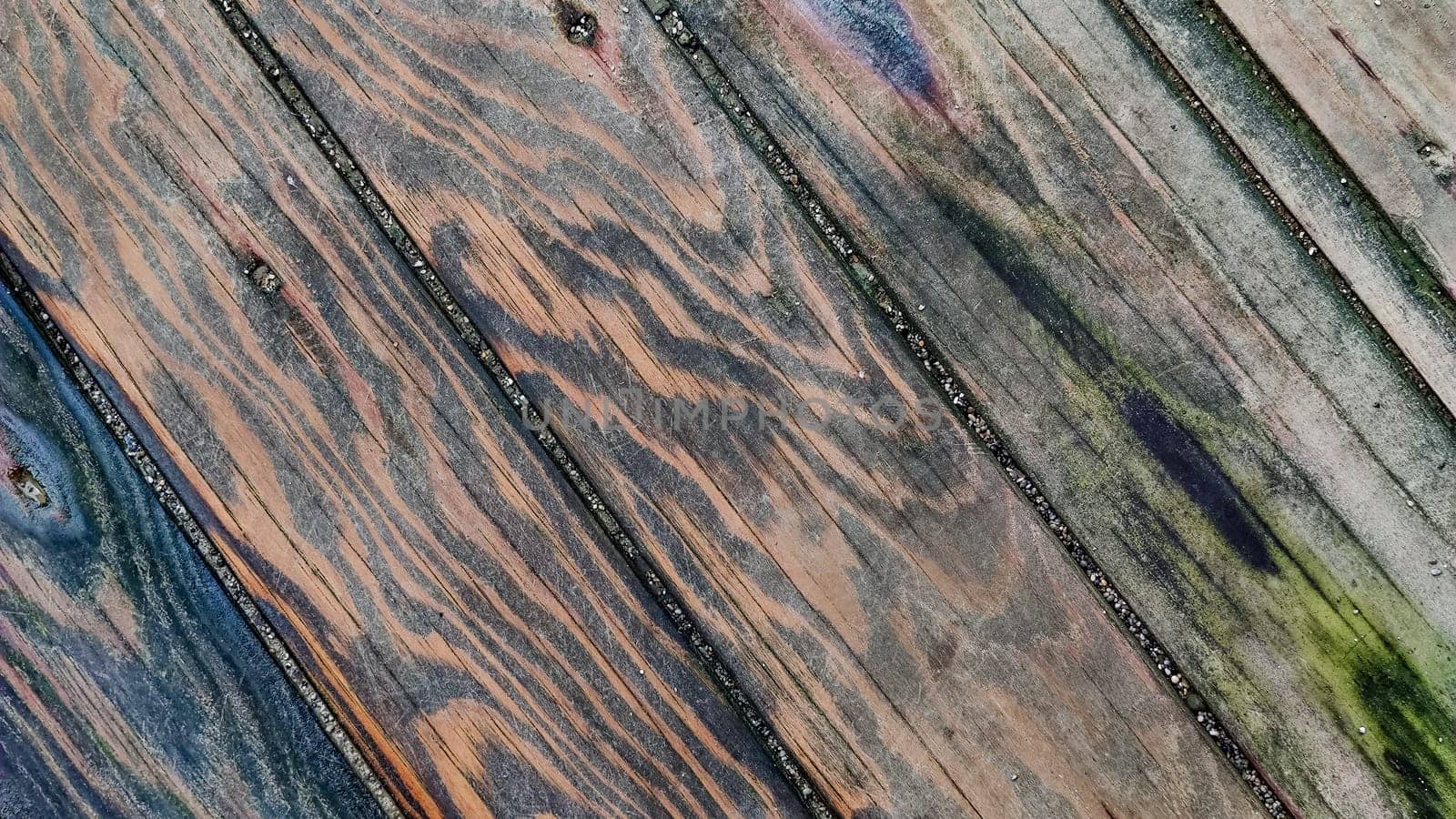 Wooden surface made of boards with multicolored spots from humidity, diagonal lines, top view, close-up.