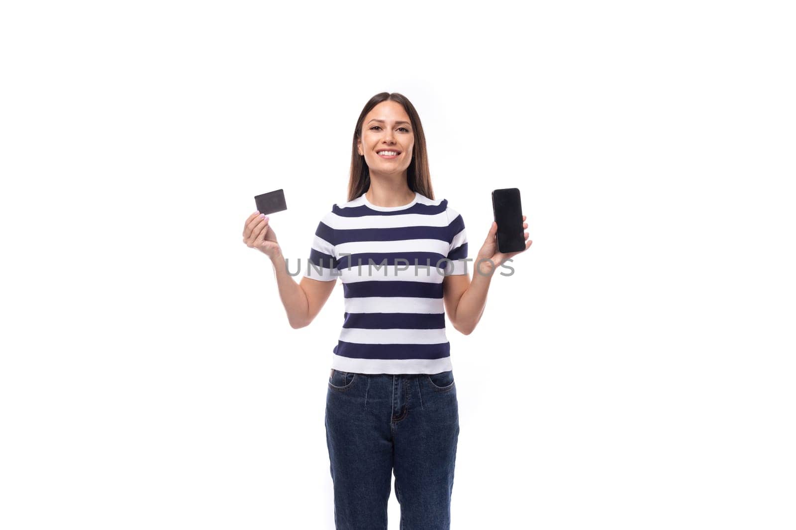 young brunette woman with straight hair dressed in a striped t-shirt holds a plastic card and a smartphone. e-business concept.
