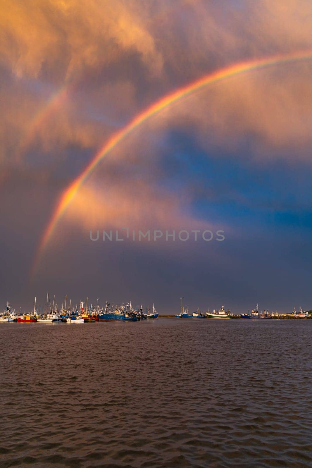 Beautiful double rainbow over the sea and coast full of small private boats right after the storm and rain at beautiful cloudy sunset at golden hour