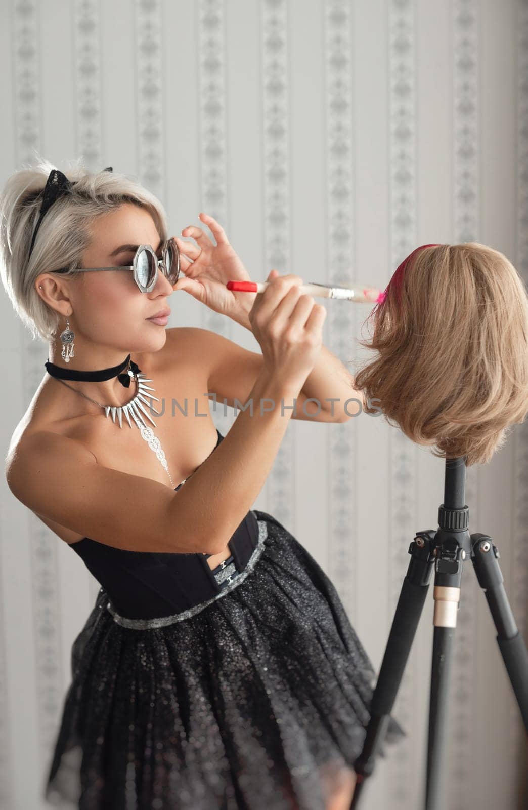 fashionable girl in stylish clothes paints her wig hair pink with a brush on the wig