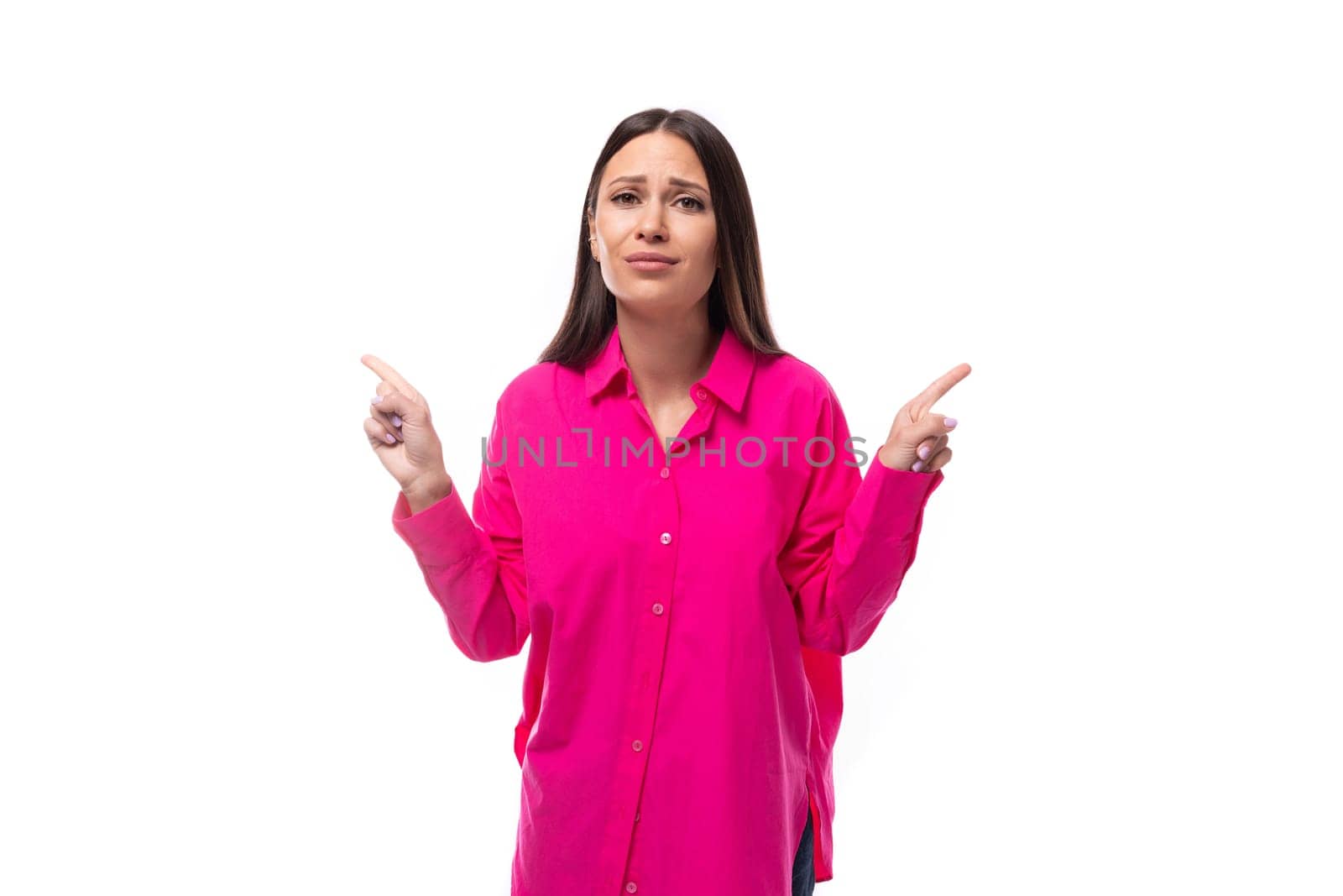 smart young brunette woman in a bright pink shirt points her finger at the space for advertising on a white background with copy space.