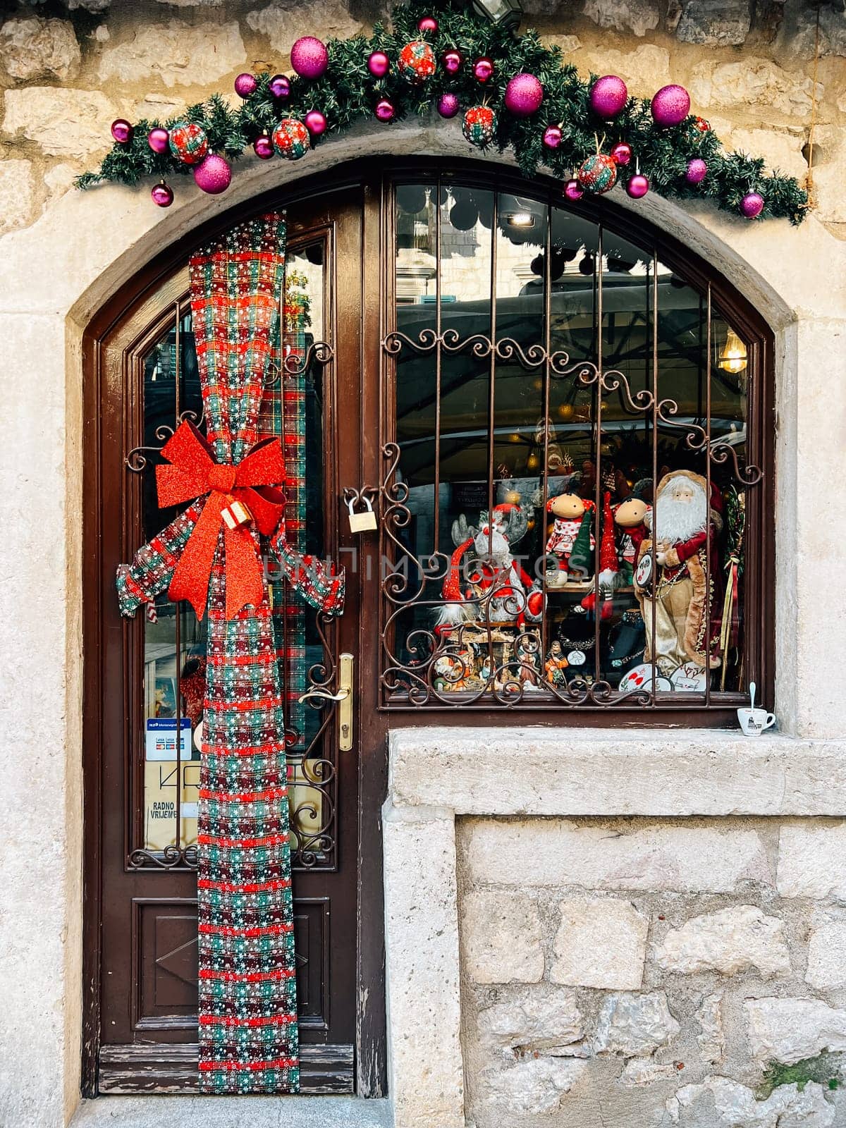 Kotor, Montenegro - 25 december 2022: Entrance to a small shop decorated with Christmas garlands and a bow by Nadtochiy