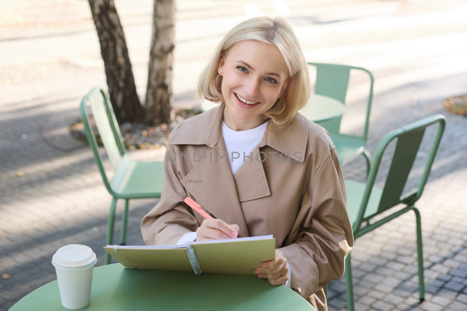 Image of young smiling woman, sitting in outdoor cafe, doing sketches, drawing art on street, spending time on coffee shop and creating art by Benzoix