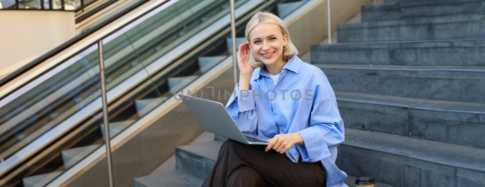 Girl student sitting on stairs in university campus, using laptop, working on project, doing homework, e-learning outdoors, drinking coffee outside, wearing stylish blue shirt by Benzoix