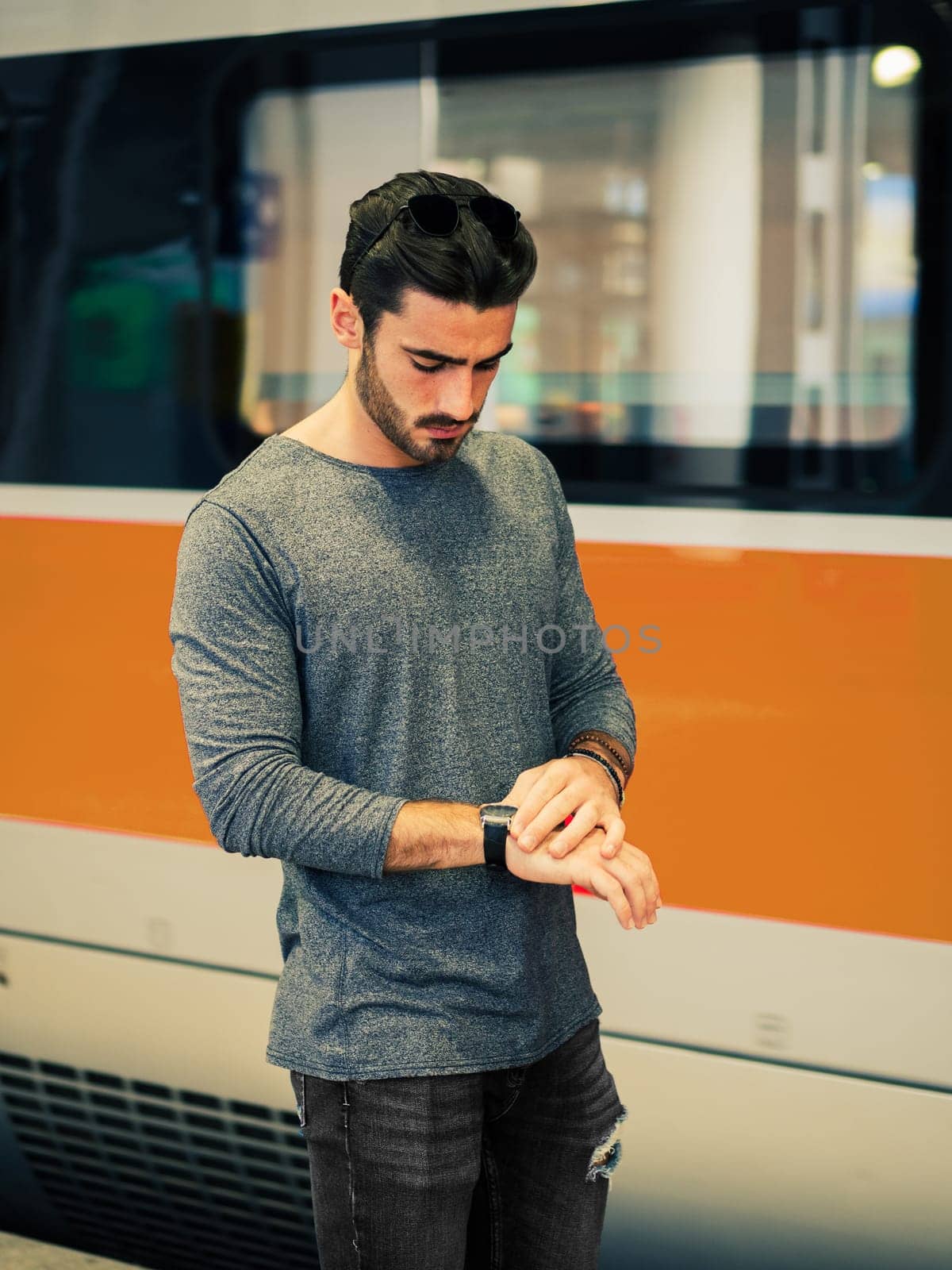 A man standing in front of a red and white train, looking at his wrist watch to check the time