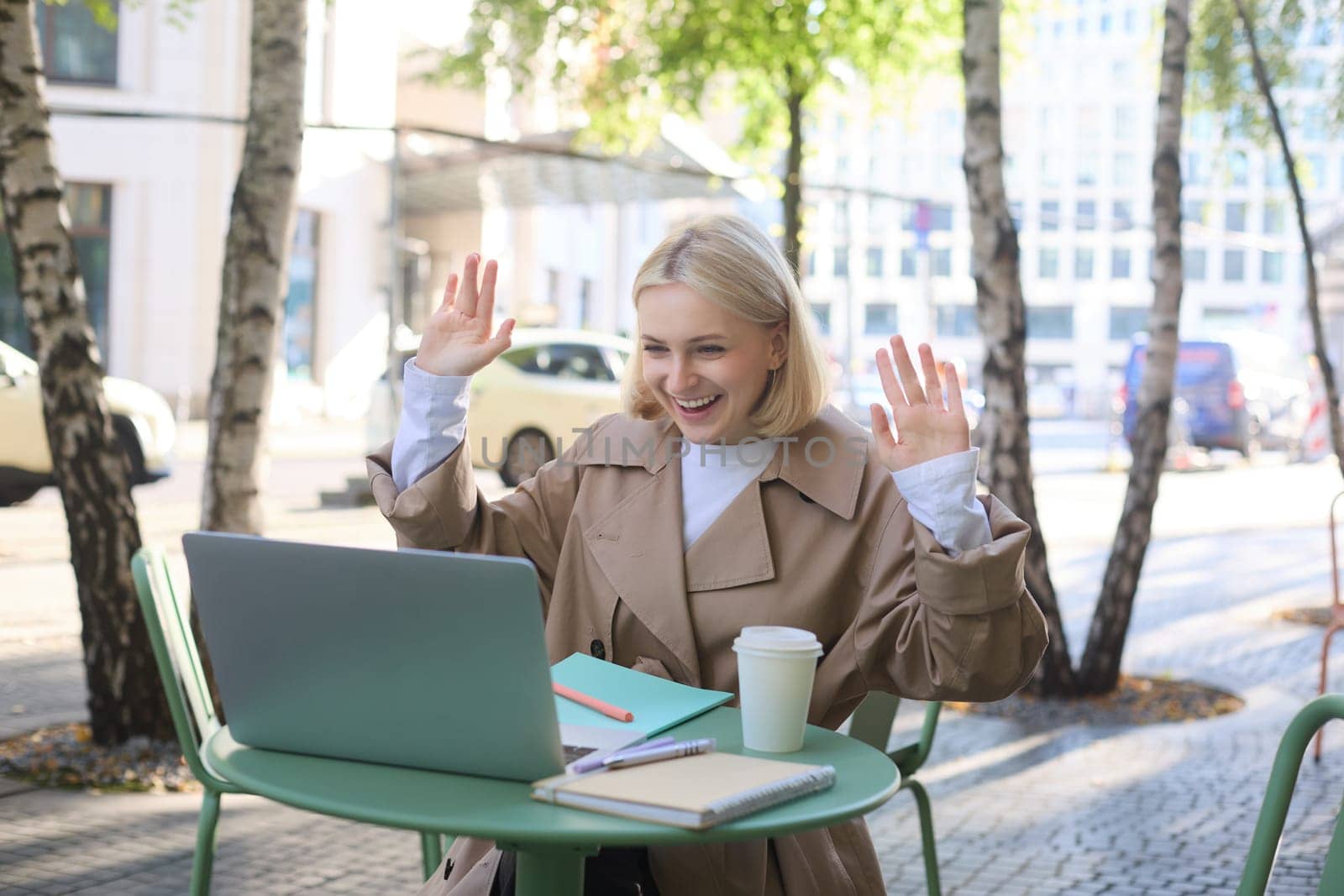 Image of excited blond girl, celebrating, sitting in coffee shop on sunny day, looking at laptop and triumphing by Benzoix