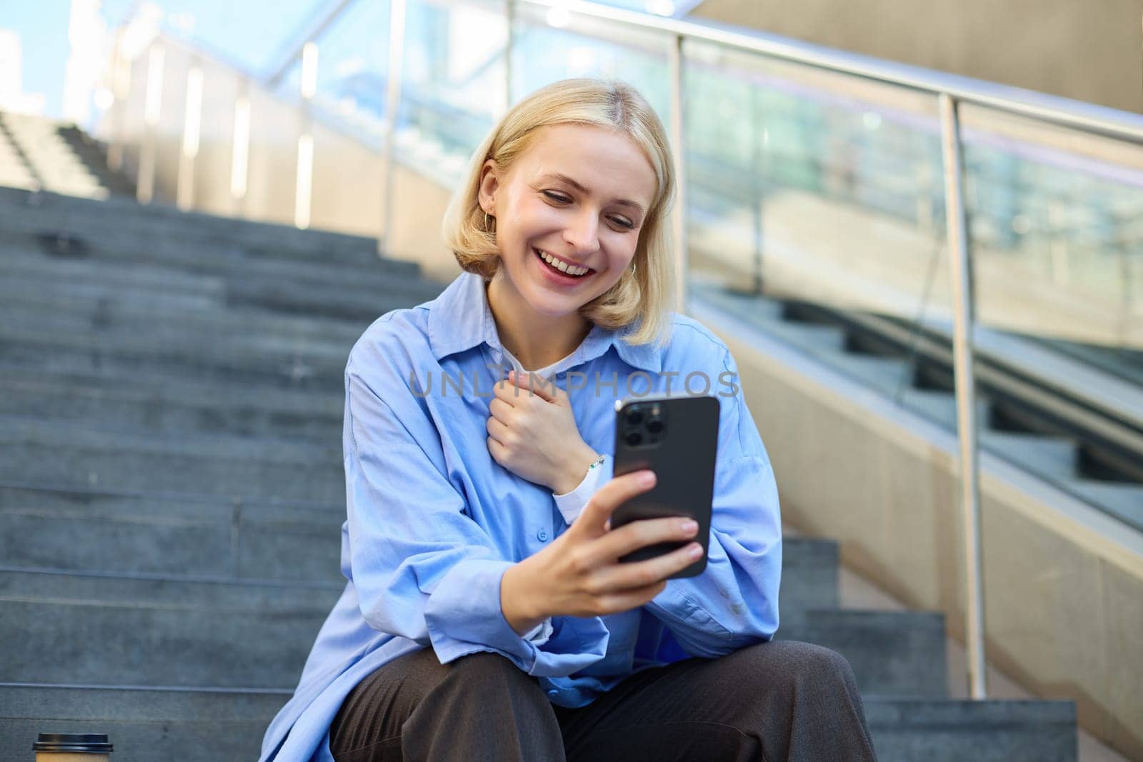 Image of young happy woman, sitting on stairs outside on street, taking selfie on smartphone camera, posing for photo social media profile, smiling.