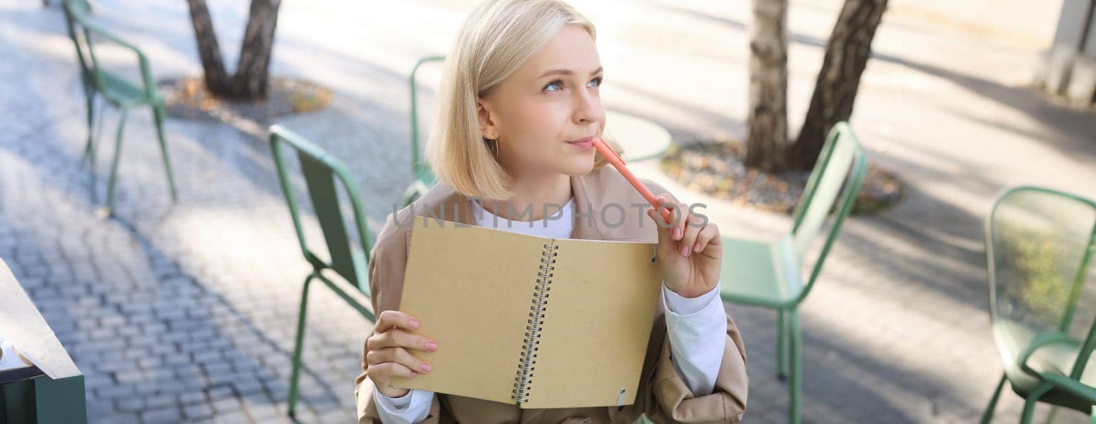 Portrait of young creative woman, doing sketches outdoors, sitting in coffee shop with notebook and pen, drawing art and smiling.